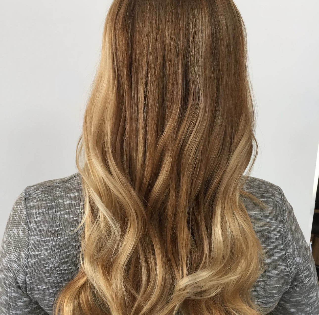 Back of a person with long, wavy, light brown hair, wearing a gray top.