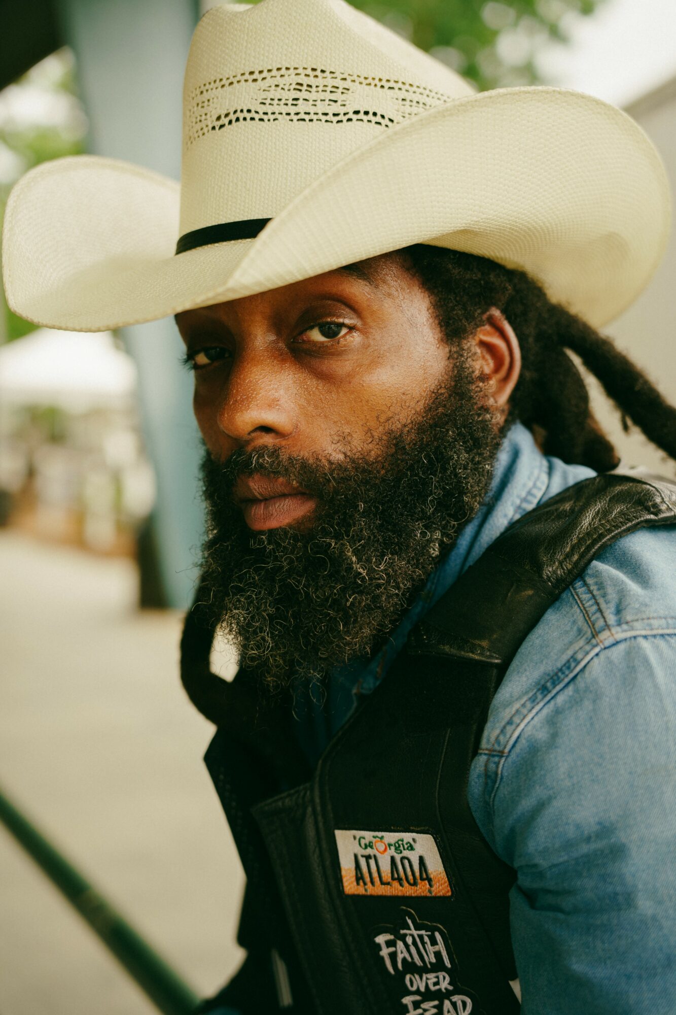 Man with a beard wearing a cowboy hat and denim jacket outdoors.