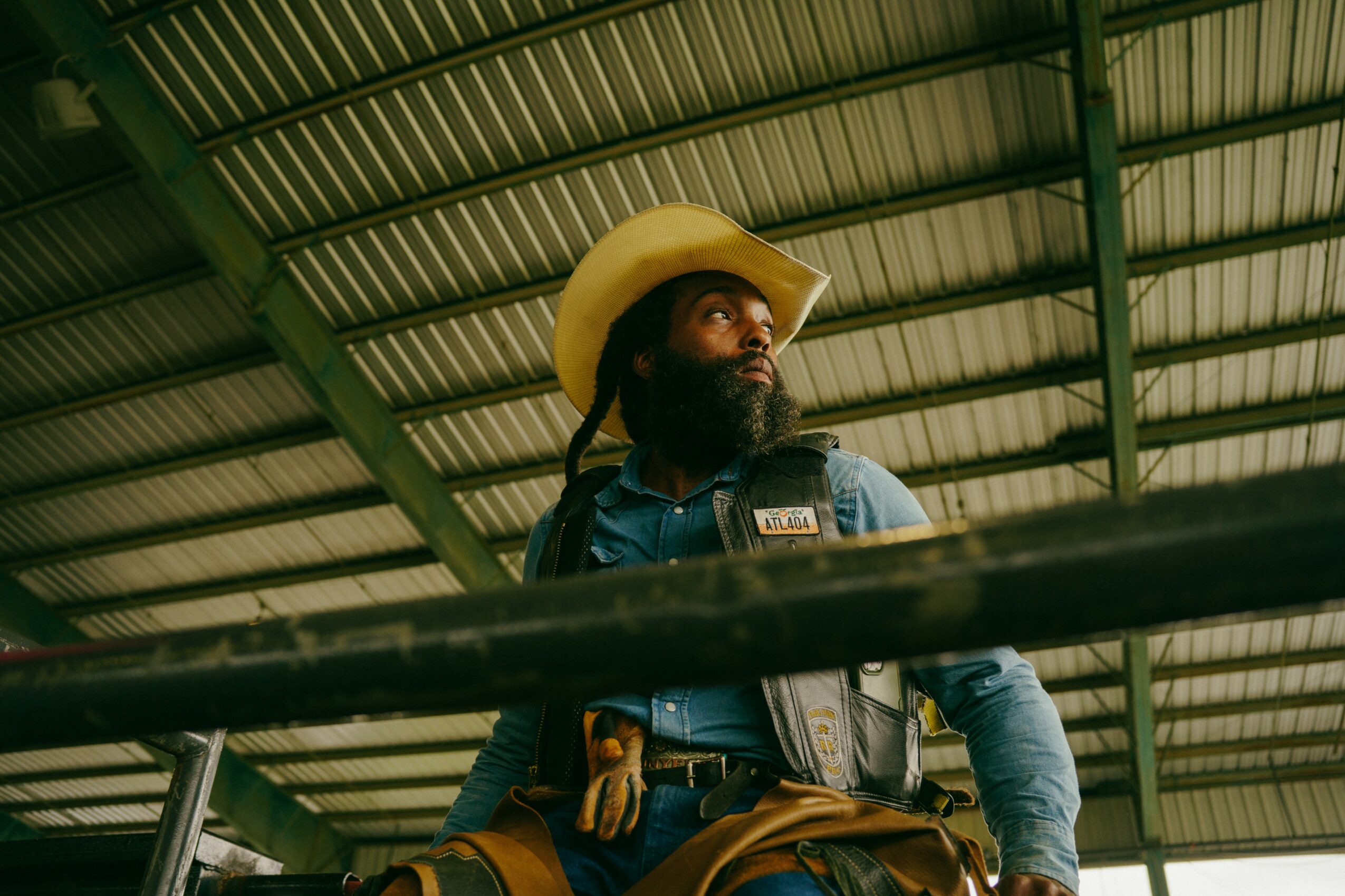 Man with a beard wearing a cowboy hat and denim shirt inside a metal structure.