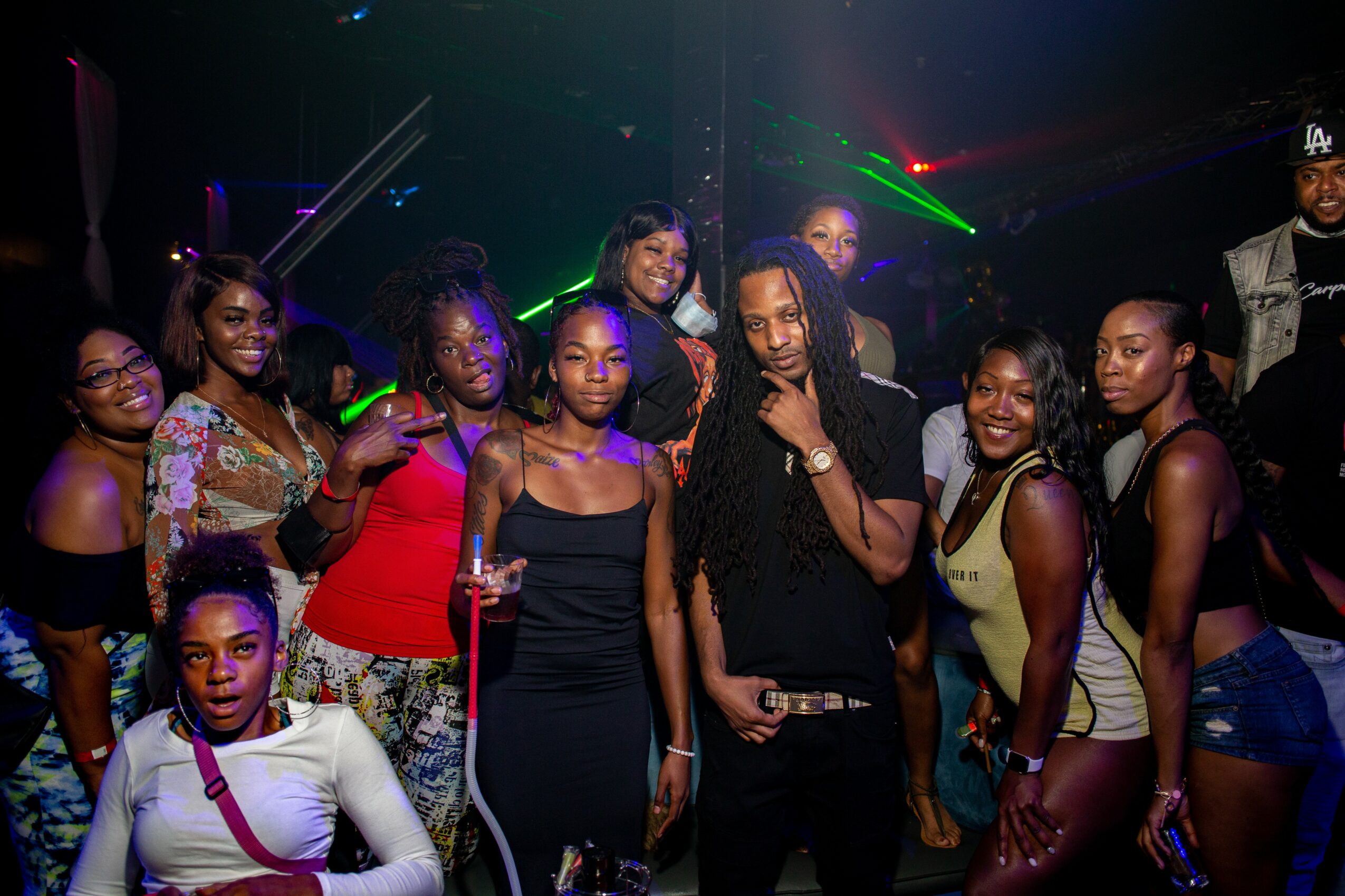 Group of people posing together in a nightclub with colorful lights and laser effects.