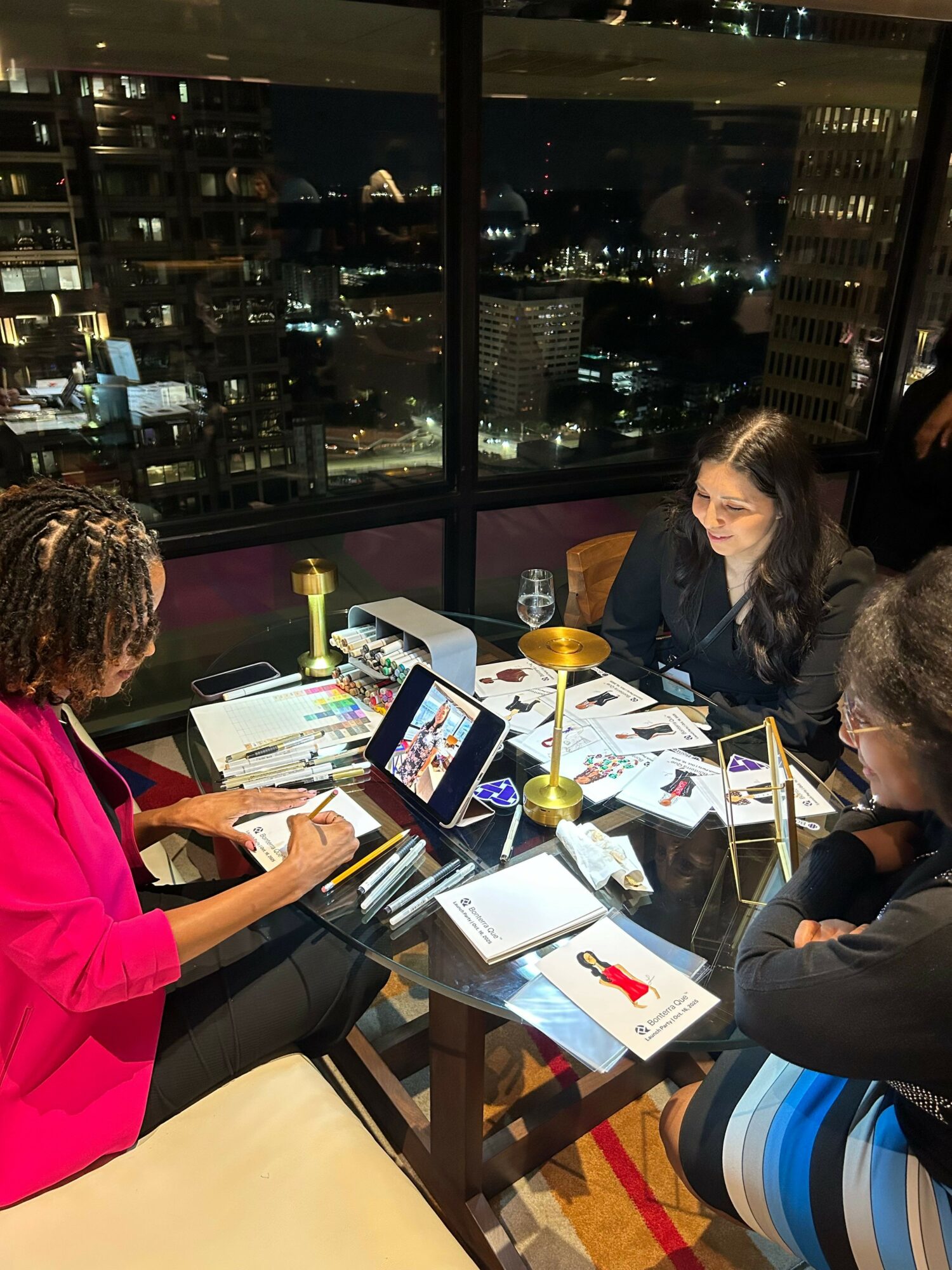 Four people sit around a table with laptops and papers, in a high-rise room overlooking a city at night.