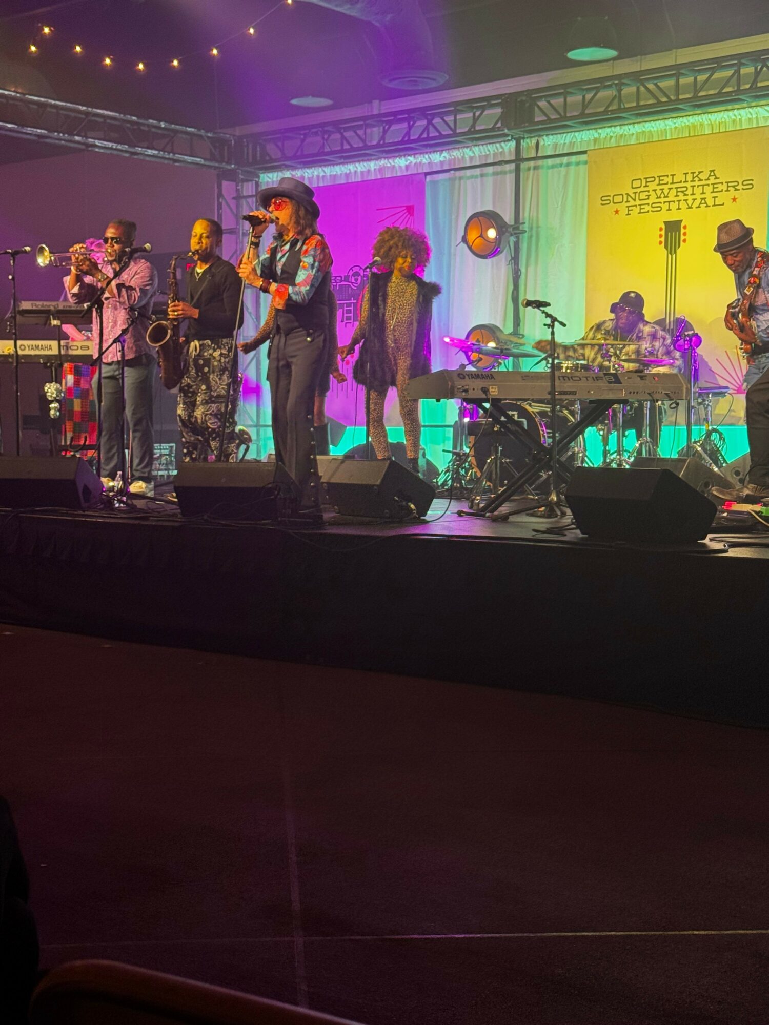 Group of musicians performing on stage with colorful lighting and a screen in the background.