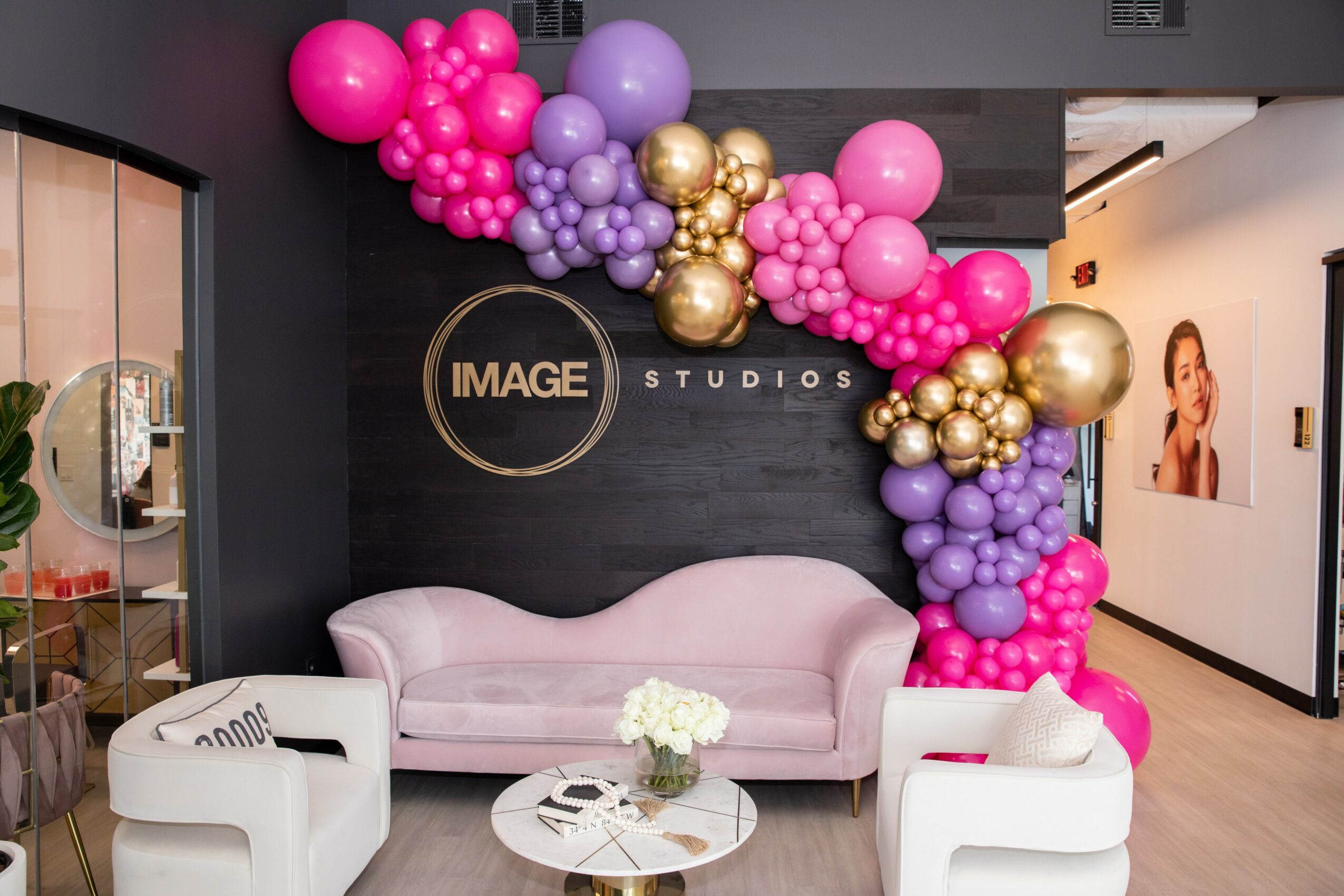 Pink, purple, and gold balloons arranged above a pink sofa in a studio setting.