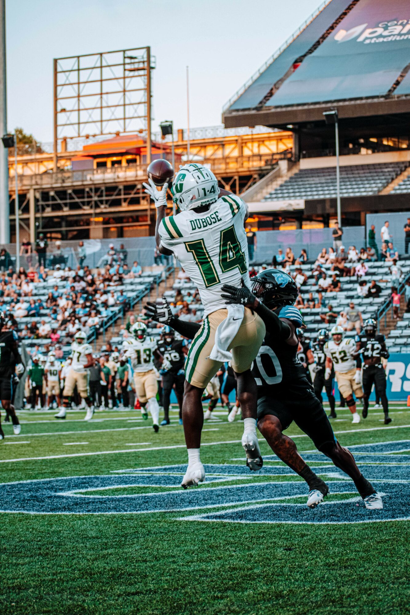 Football player in white uniform catches ball while opposing player reaches for him on field.