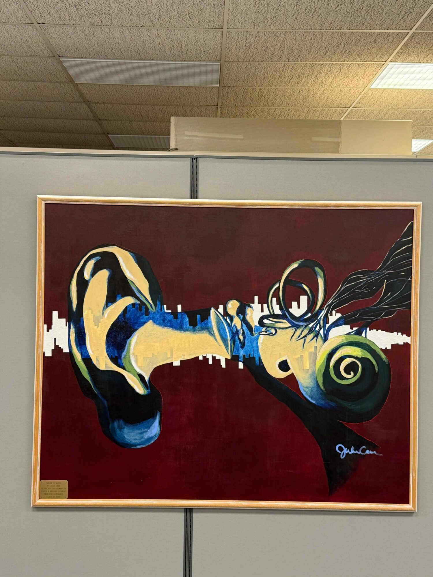 Abstract painting with swirling shapes and bold colors on a red background, framed and hung on a wall.