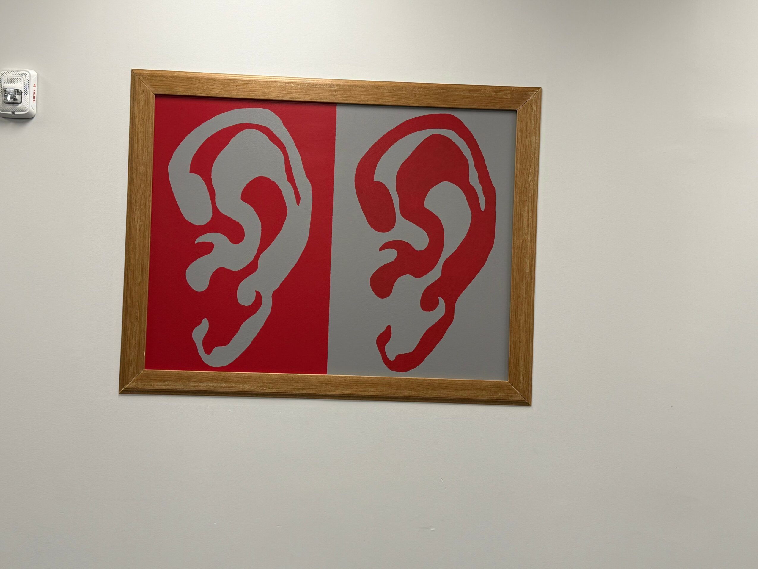 Framed artwork with two stylized ear illustrations, one on a red background and the other on a gray background.