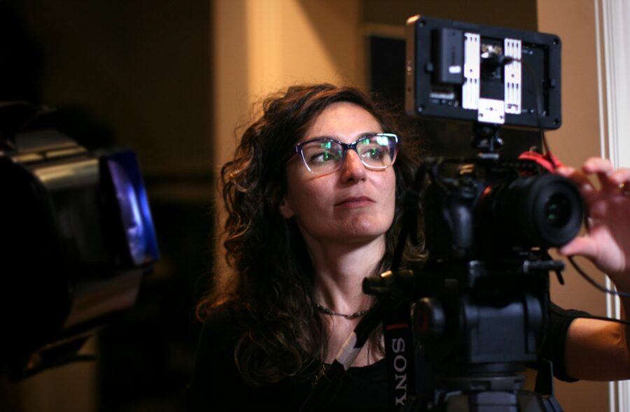 Woman with glasses operating a professional camera in an indoor setting.
