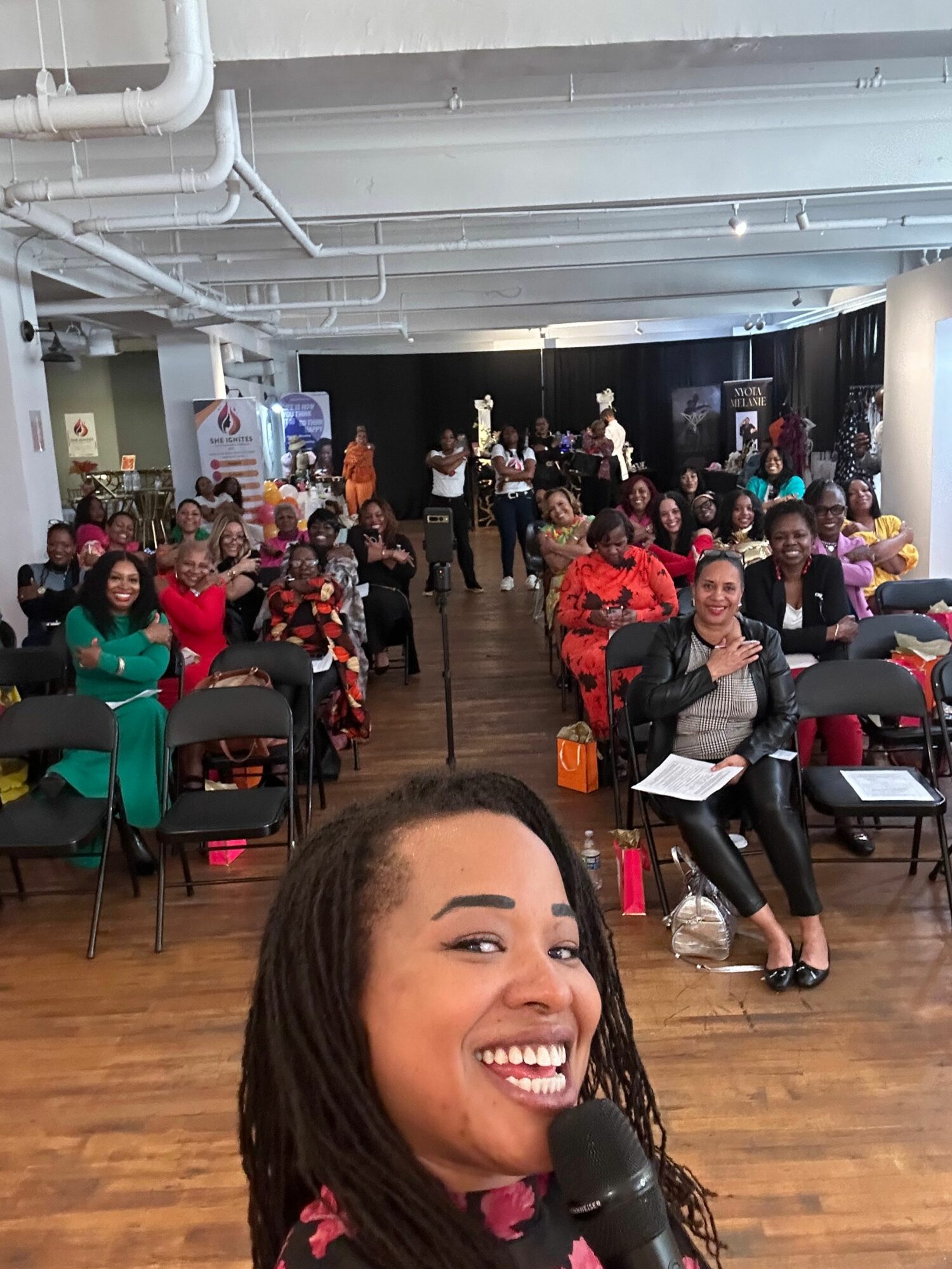 Woman with long hair smiling and holding a microphone in a large indoor gathering.