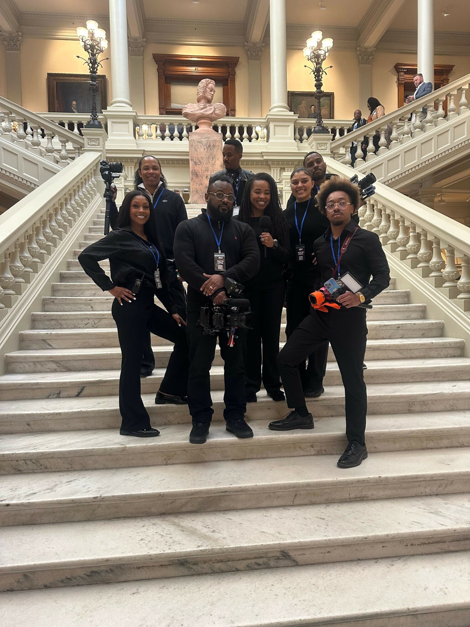 Group of seven people standing on marble staircase in elegant building, posing for photo.