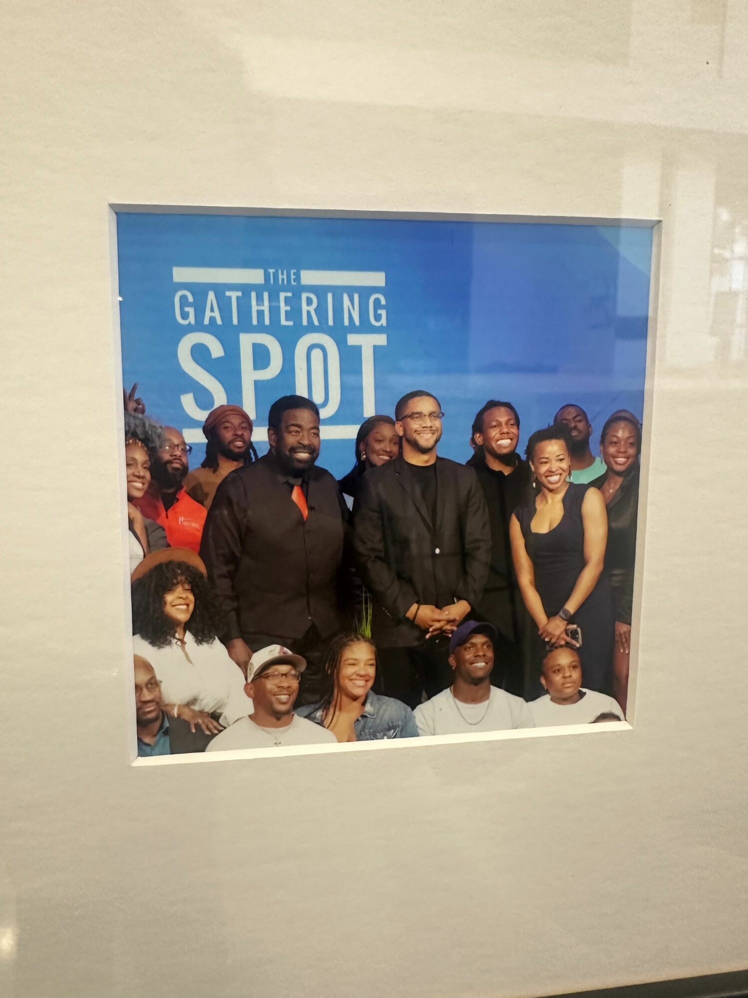 Group of people smiling in front of a blue background with text, some wearing glasses and casual clothing.