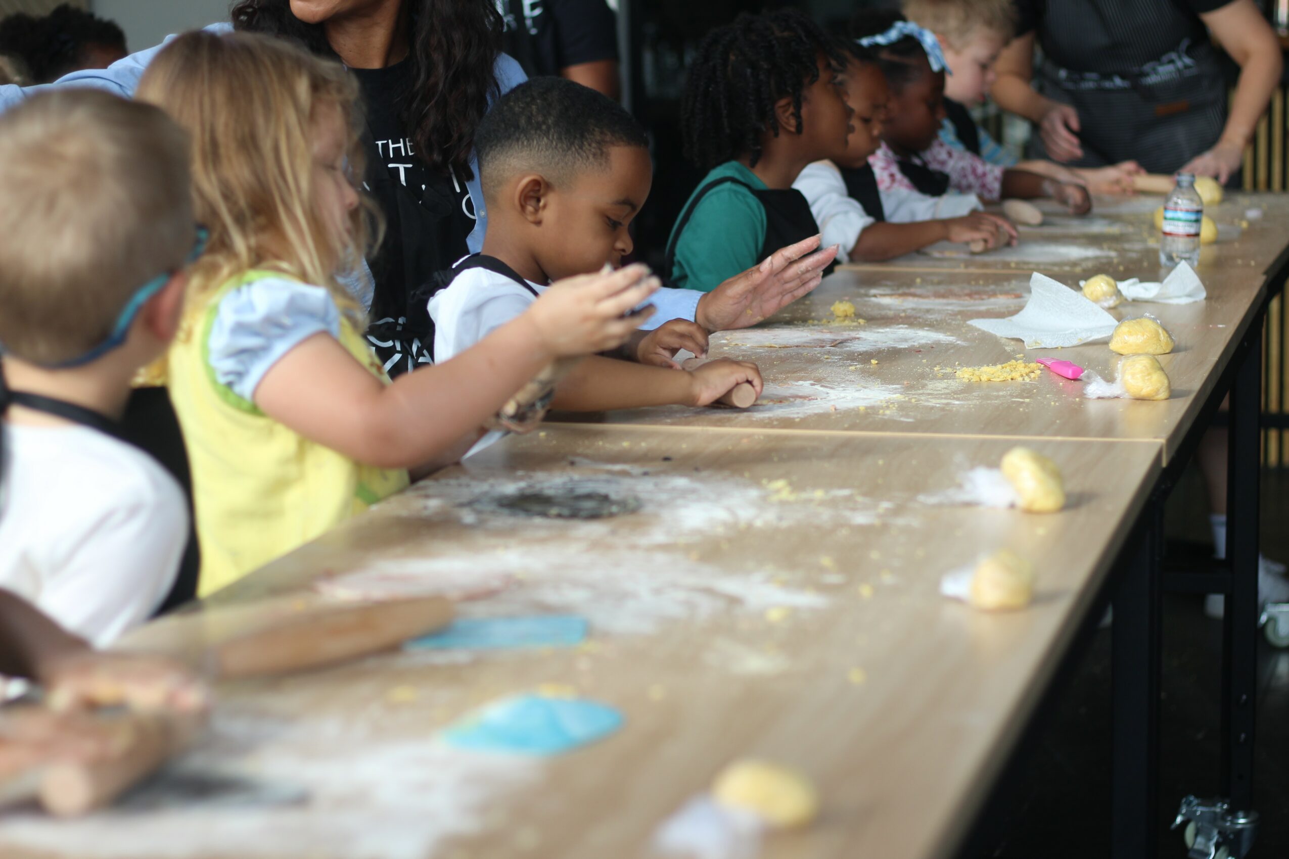 Children gathered around a table, engaging in a baking activity with dough and ingredients.