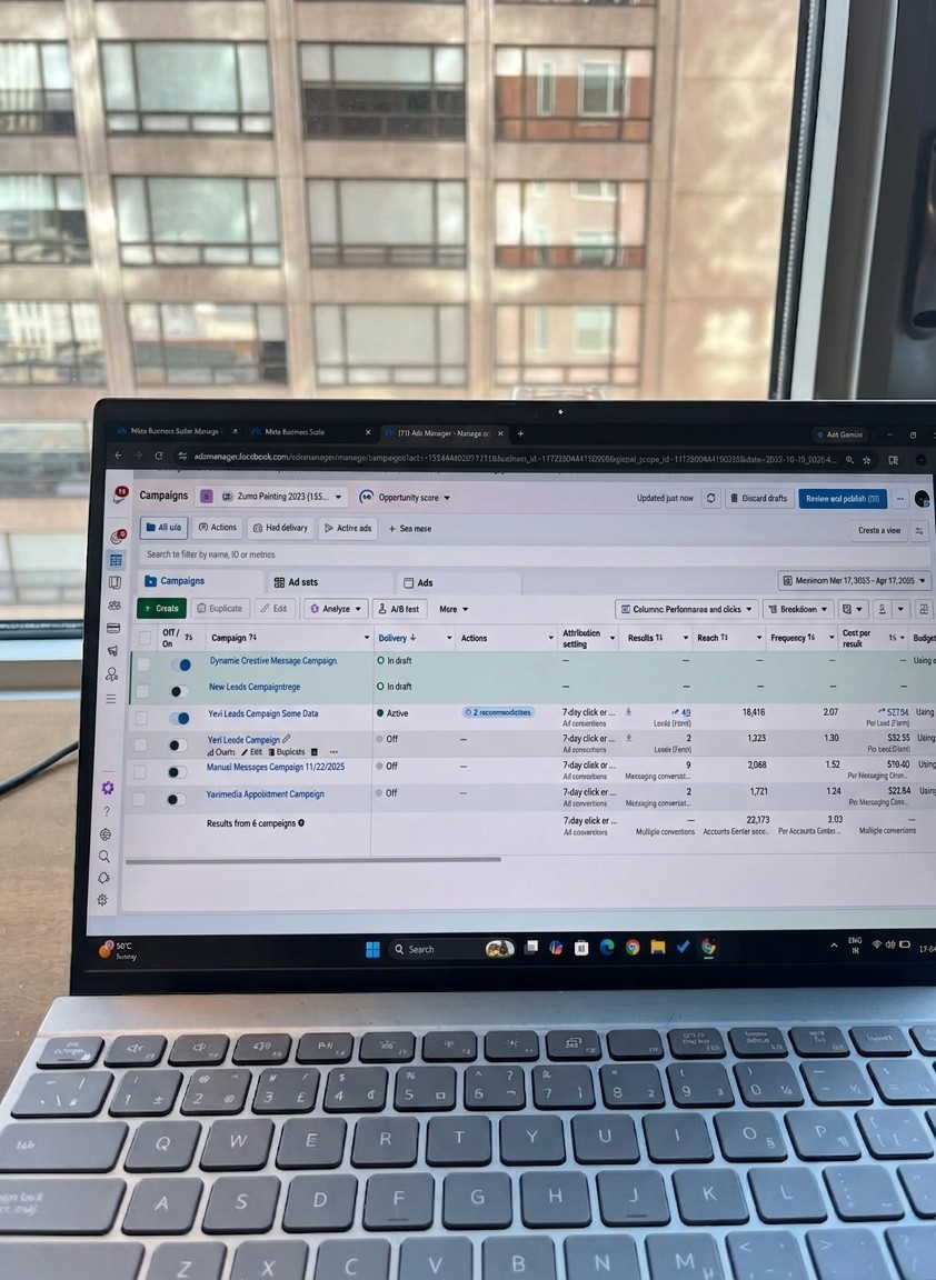Laptop screen displaying a spreadsheet or database, with a window showing a building outside in the background.