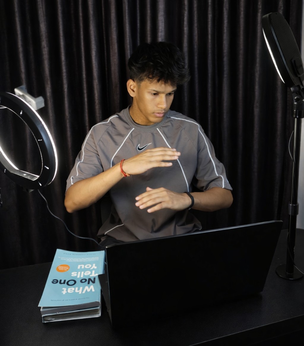 Young person with dark hair using a laptop, surrounded by studio lights, with a dark curtain background.