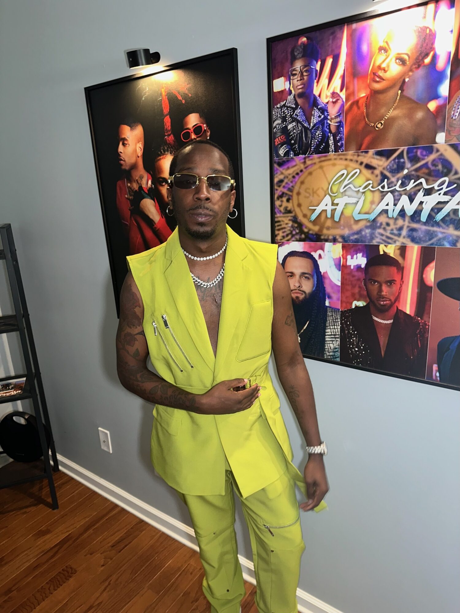 Person wearing yellow suit and sunglasses standing indoors with colorful posters behind them.