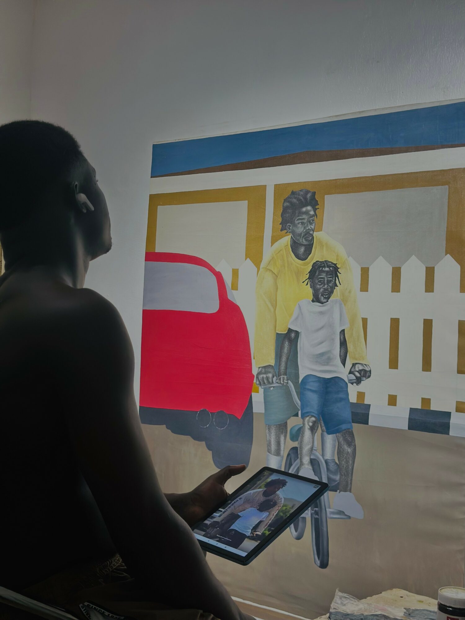 Person holding a tablet in front of a mural with two children and a red vehicle.