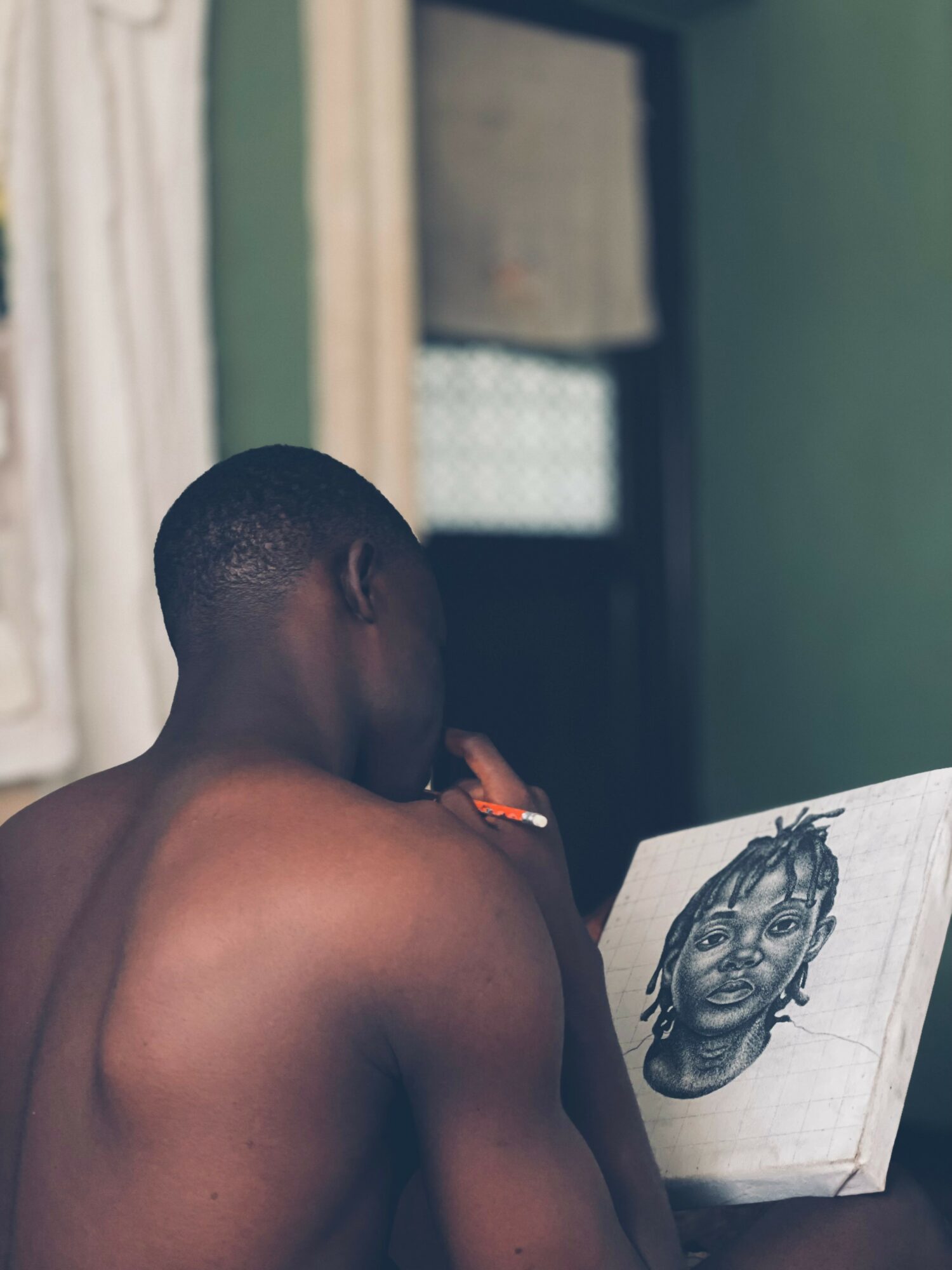 Person with short hair looking at a drawing of a woman with braided hair, in a room with green walls.