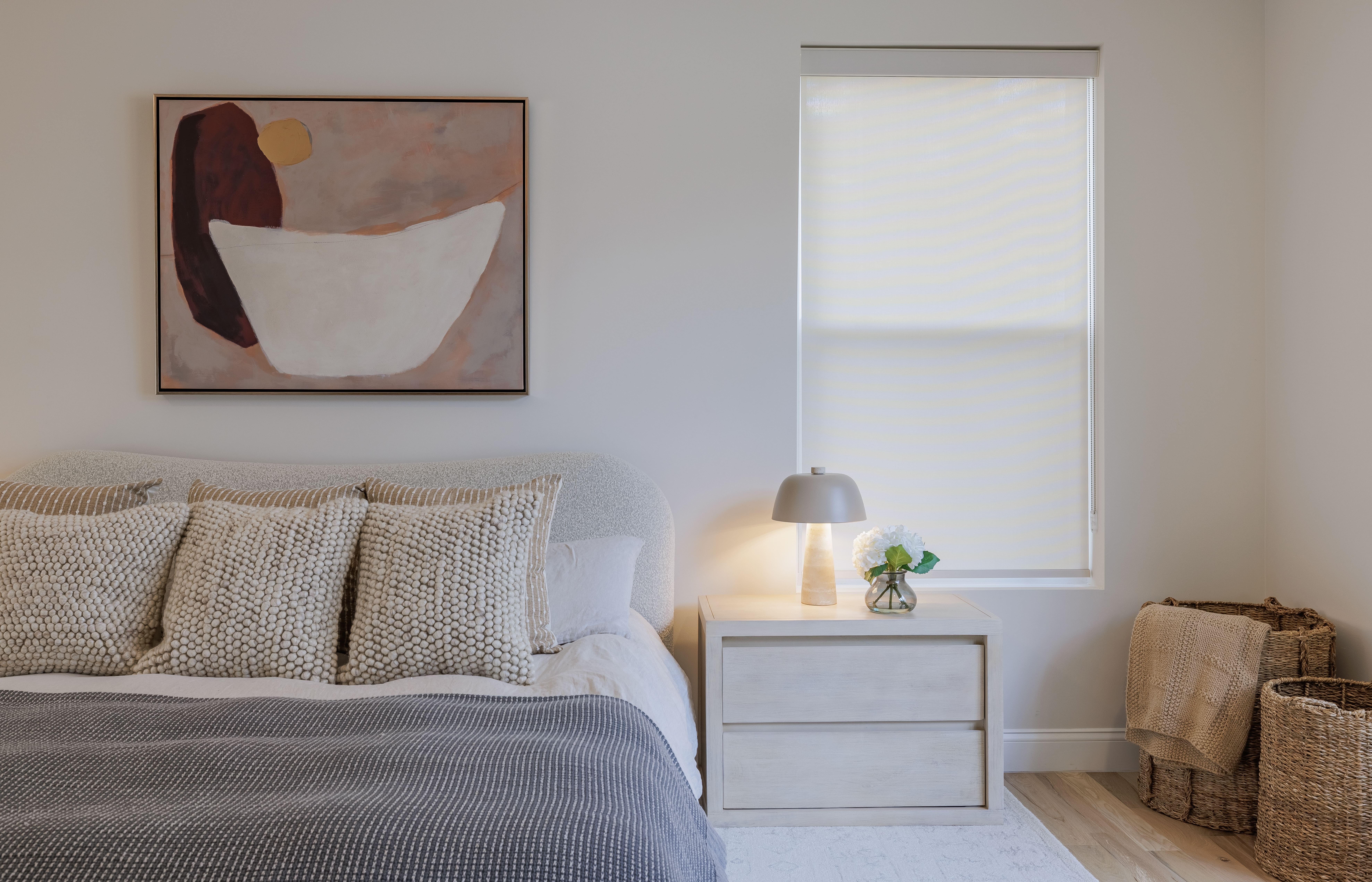 Bedroom with bed, pillows, nightstand, lamp, window, and basket in corner.