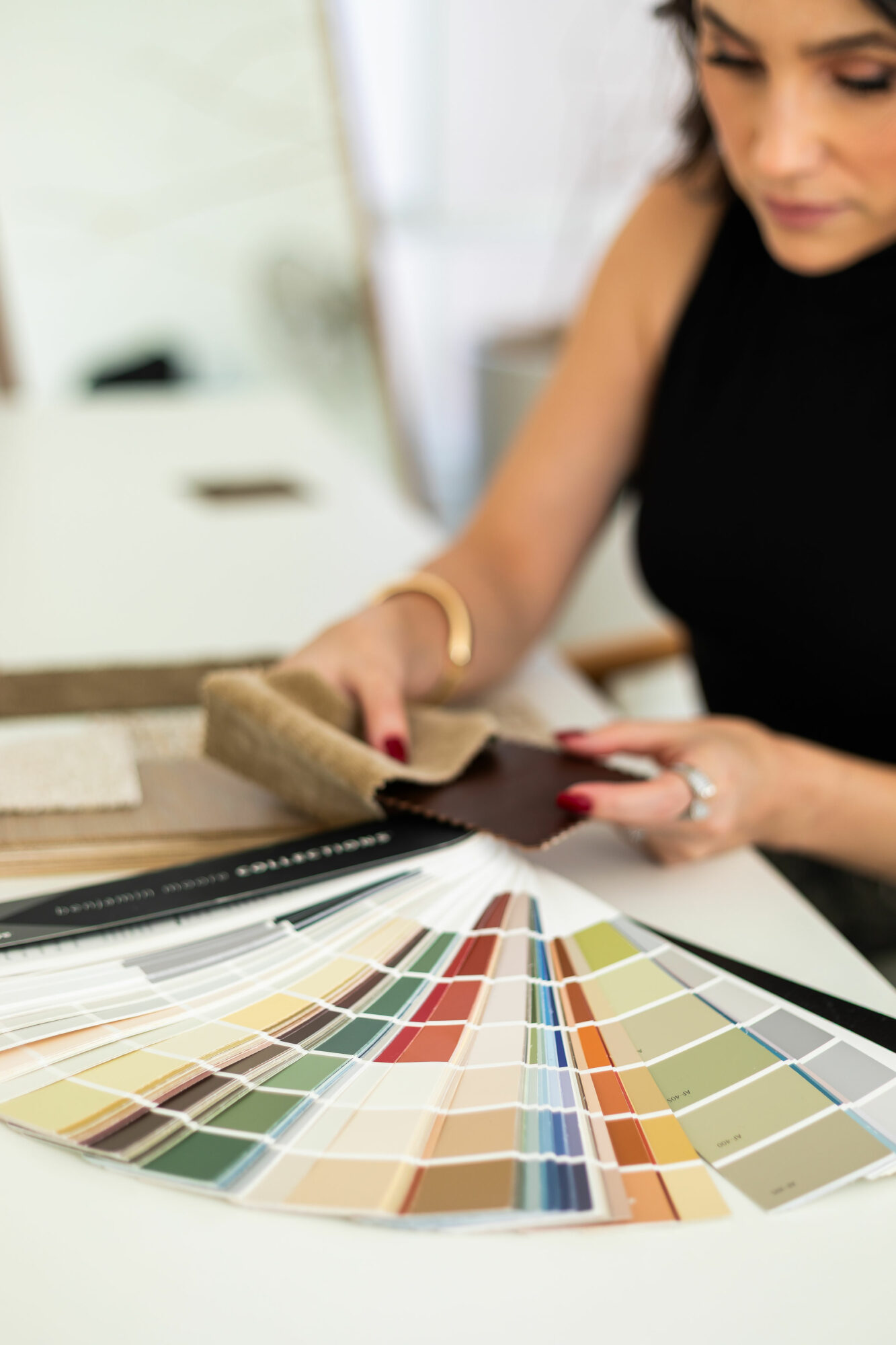 Person selecting fabric swatches with color samples and a color palette fan deck on table.