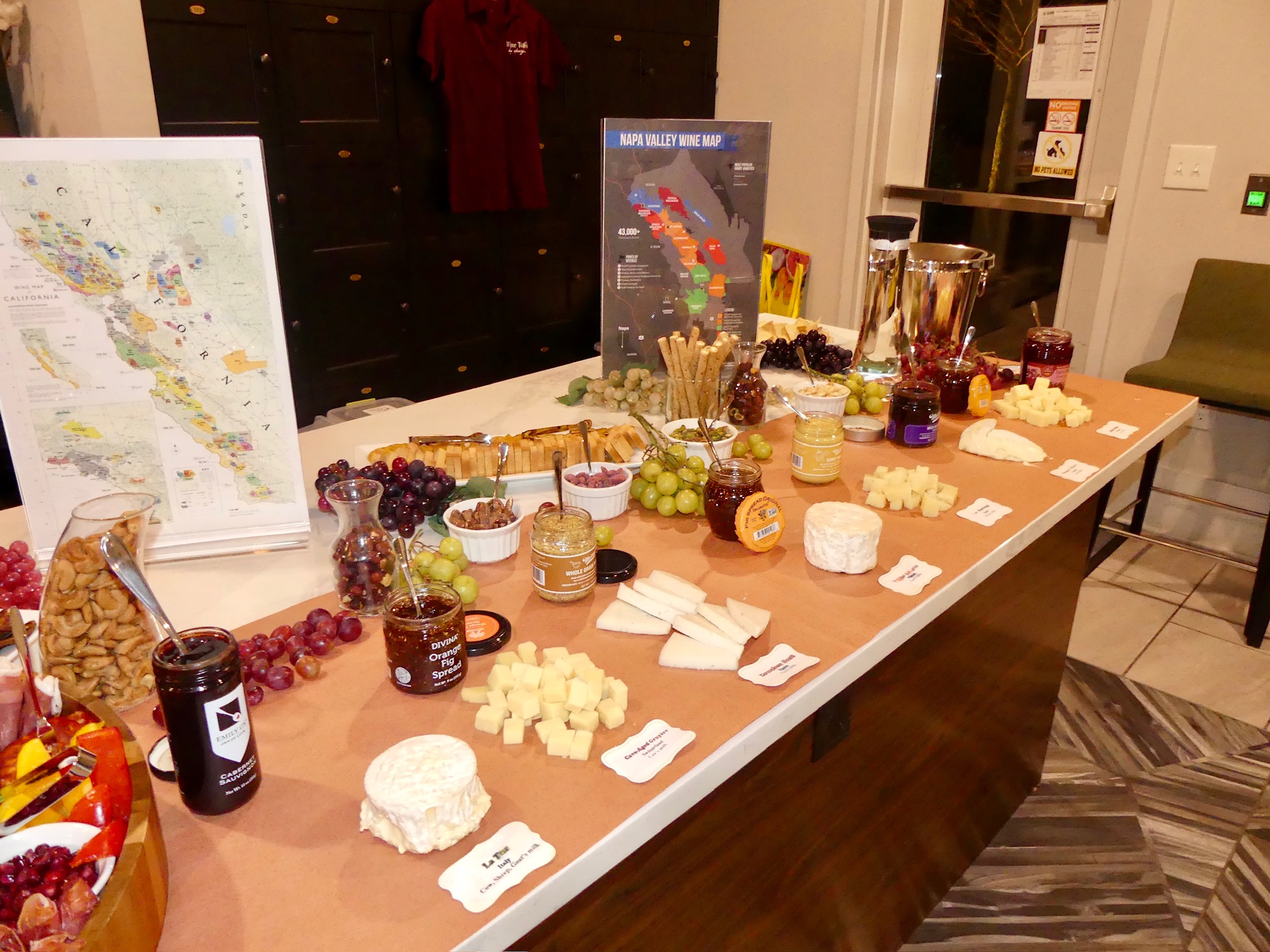 Table with various jars, bowls, and plates of food, drinks, and snacks in a room with maps and posters on the wall.