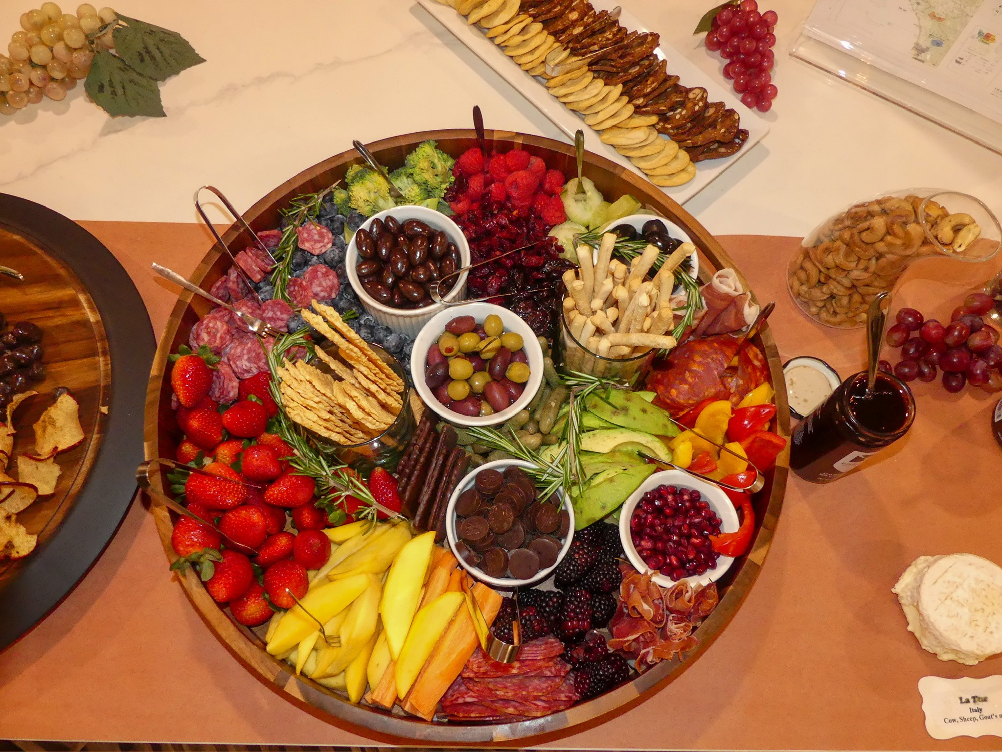 Assorted fruits, berries, nuts, and cheeses on a round platter with small bowls of toppings.