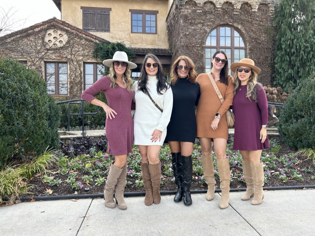 Five women standing outdoors in front of a garden and historic building, posing for a group photo.
