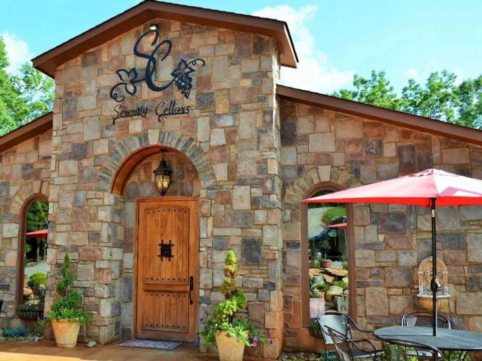 Stone building with wooden door, outdoor seating with umbrella, potted plants, and a sign with a snake and grapes.