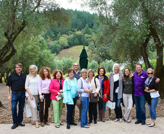 Group of fifteen people standing outdoors on a dirt path with trees and greenery in background.
