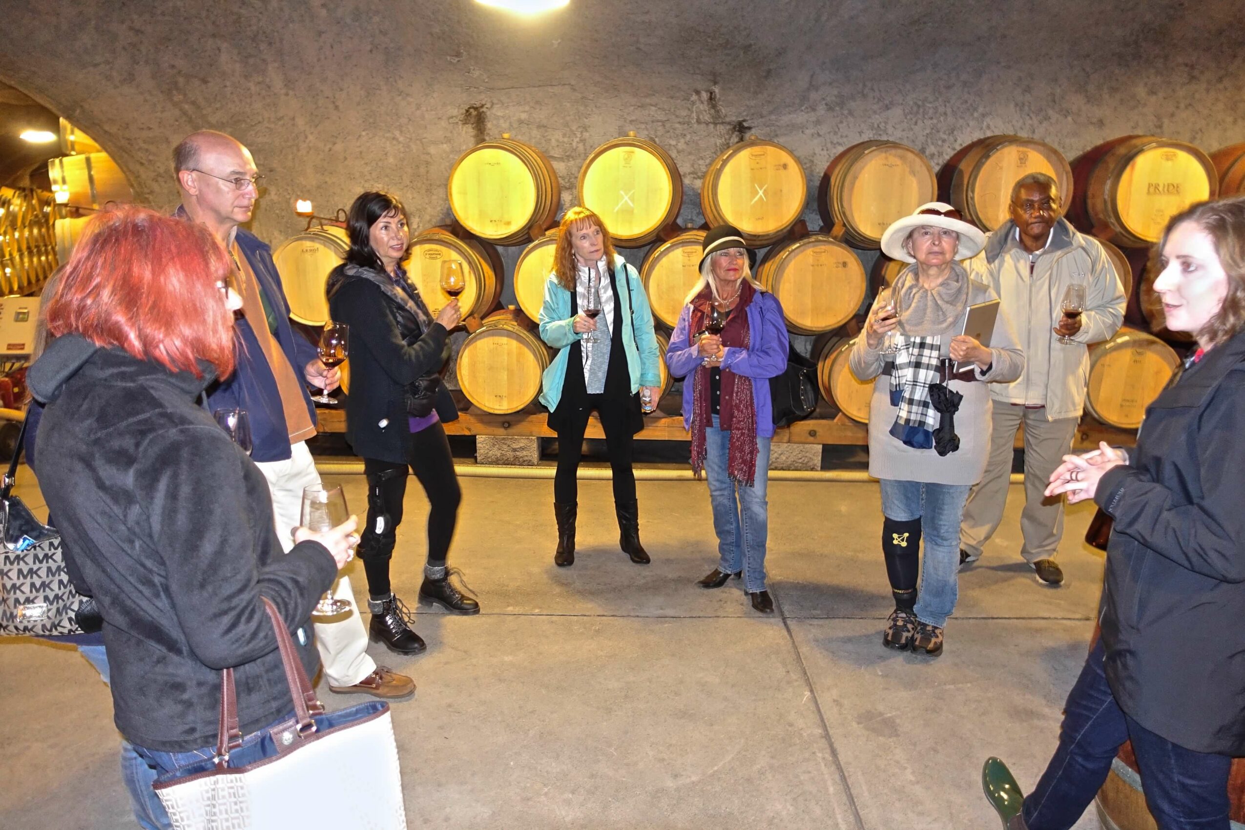 Group of people standing and talking indoors with large barrels in the background.