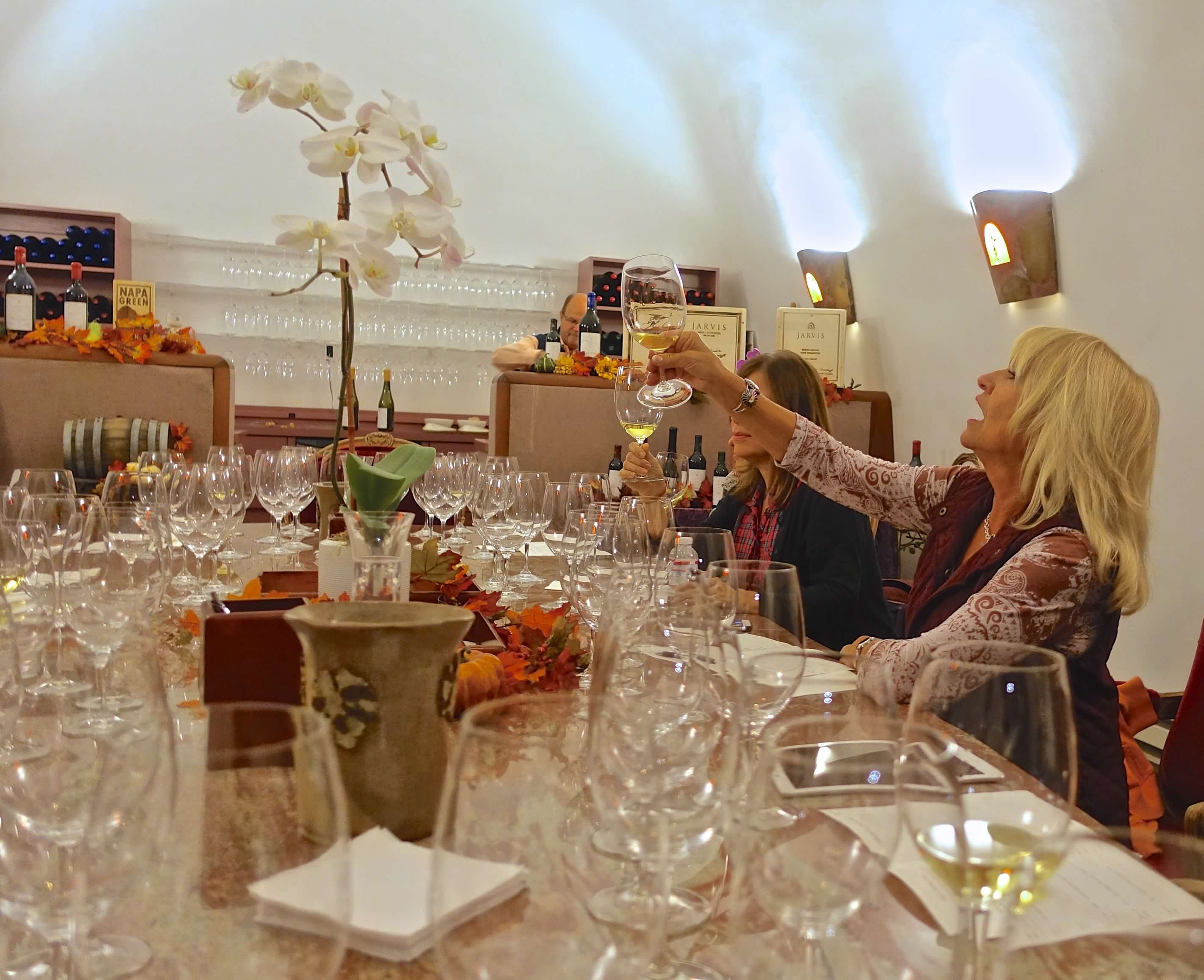 People sitting at a table with glasses, bottles, and a flower arrangement, raising glasses in a toast.