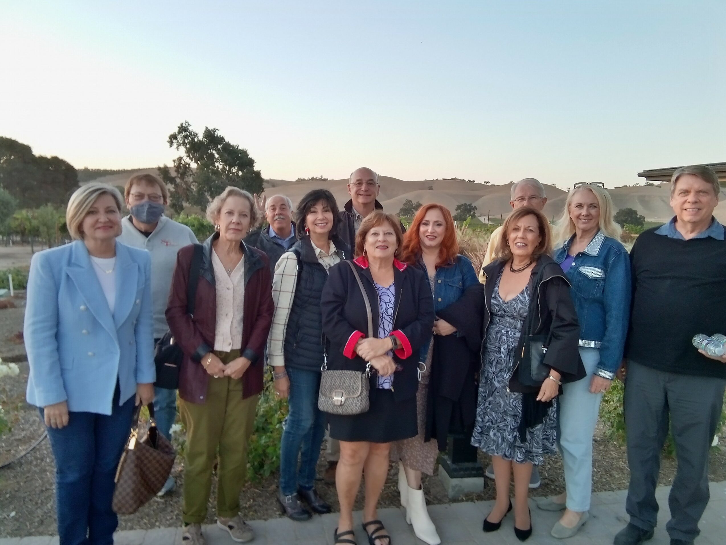 Group of ten people standing outdoors with greenery and hills in the background, smiling at the camera.