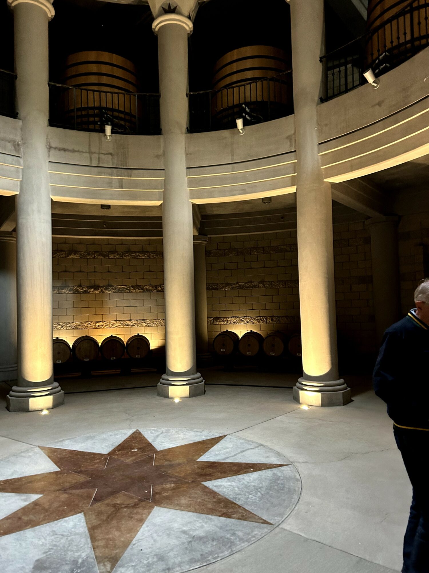 Interior view with tall columns, barrels against a brick wall, and a person partially visible on the right.