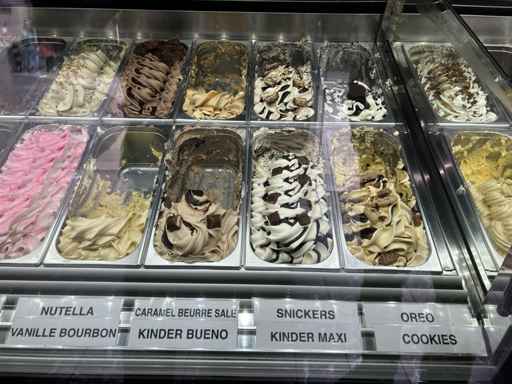 Ice cream flavors in a display case with labels including Nutella, Kinder Bueno, Snickers, Oreo, Cookies, and others.