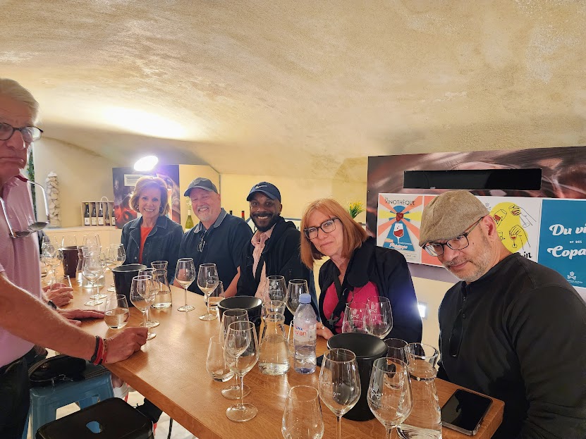 Group of six people sitting at a bar counter with glasses and drinks, smiling and engaging with each other.