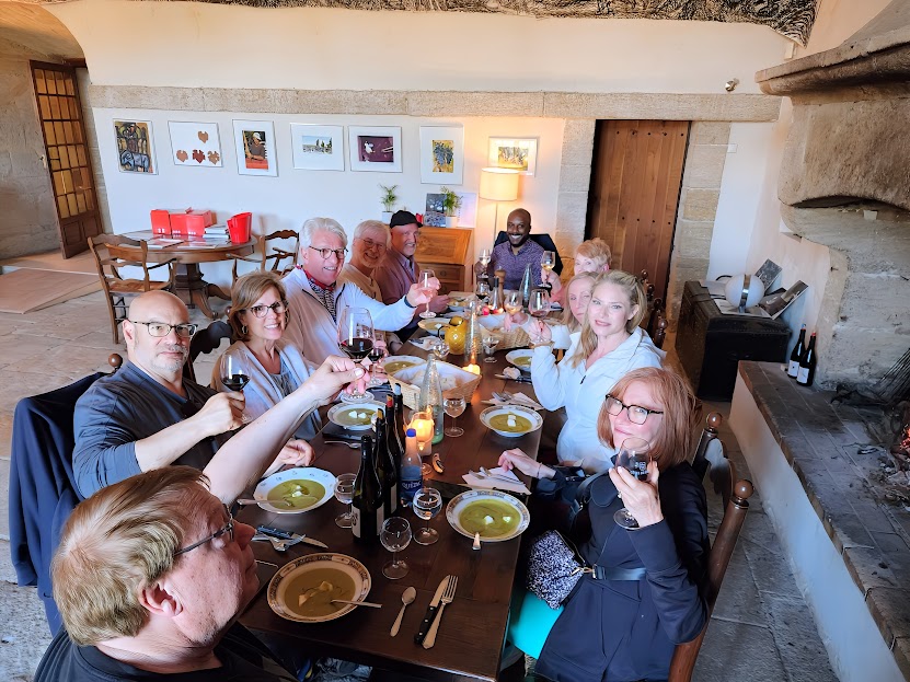 Group of ten people sitting around a dining table with food and drinks in a cozy room with artwork on the wall.