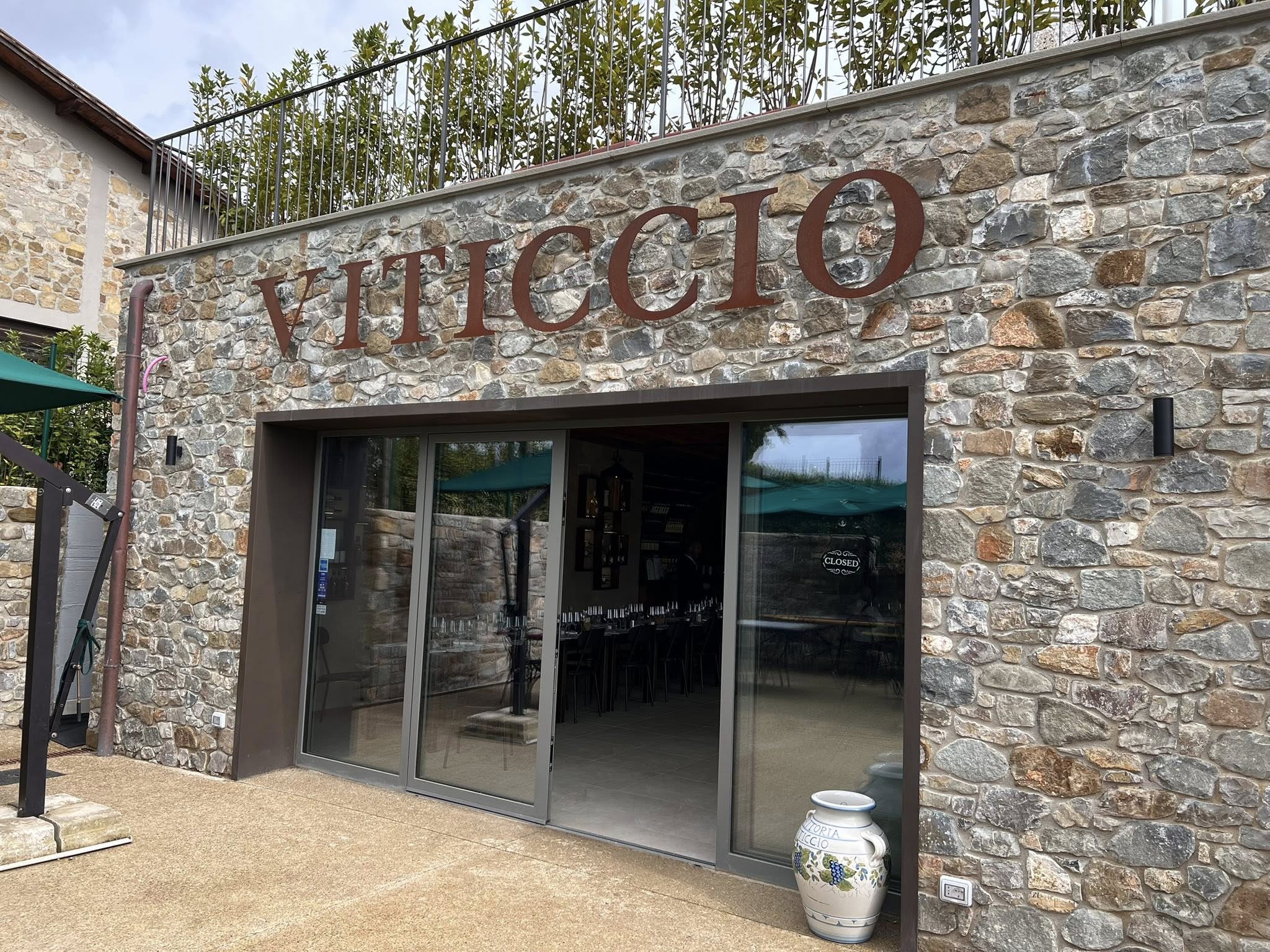 Stone building with large glass doors and the word 'VITICCIO' on the wall above.