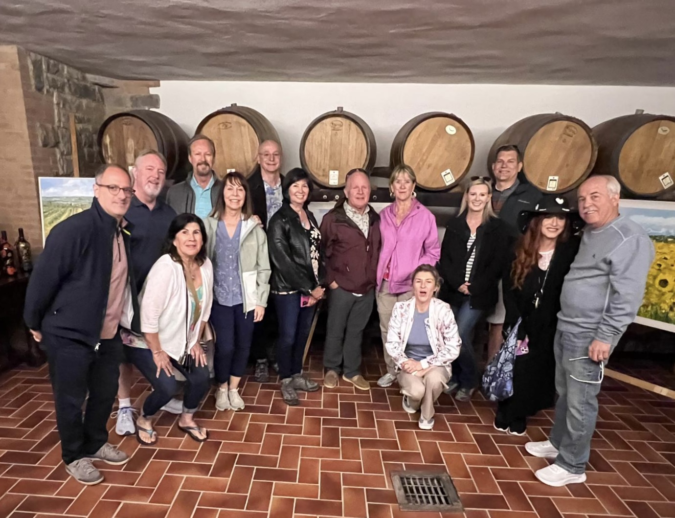 Group of people standing in a wine cellar with large barrels on the wall behind them.