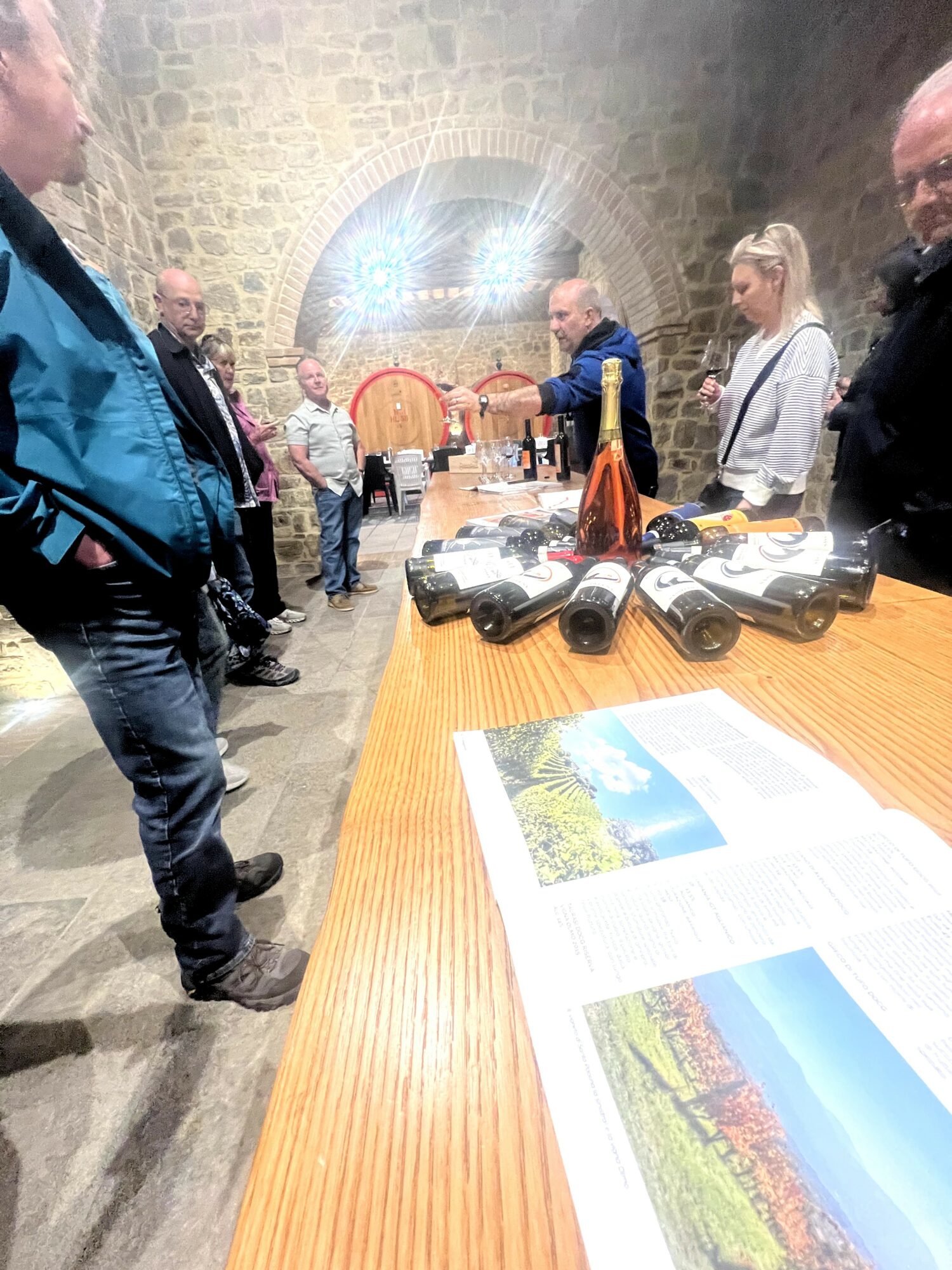 Group of people gathered around a table with binoculars and a brochure in a stone-walled room.