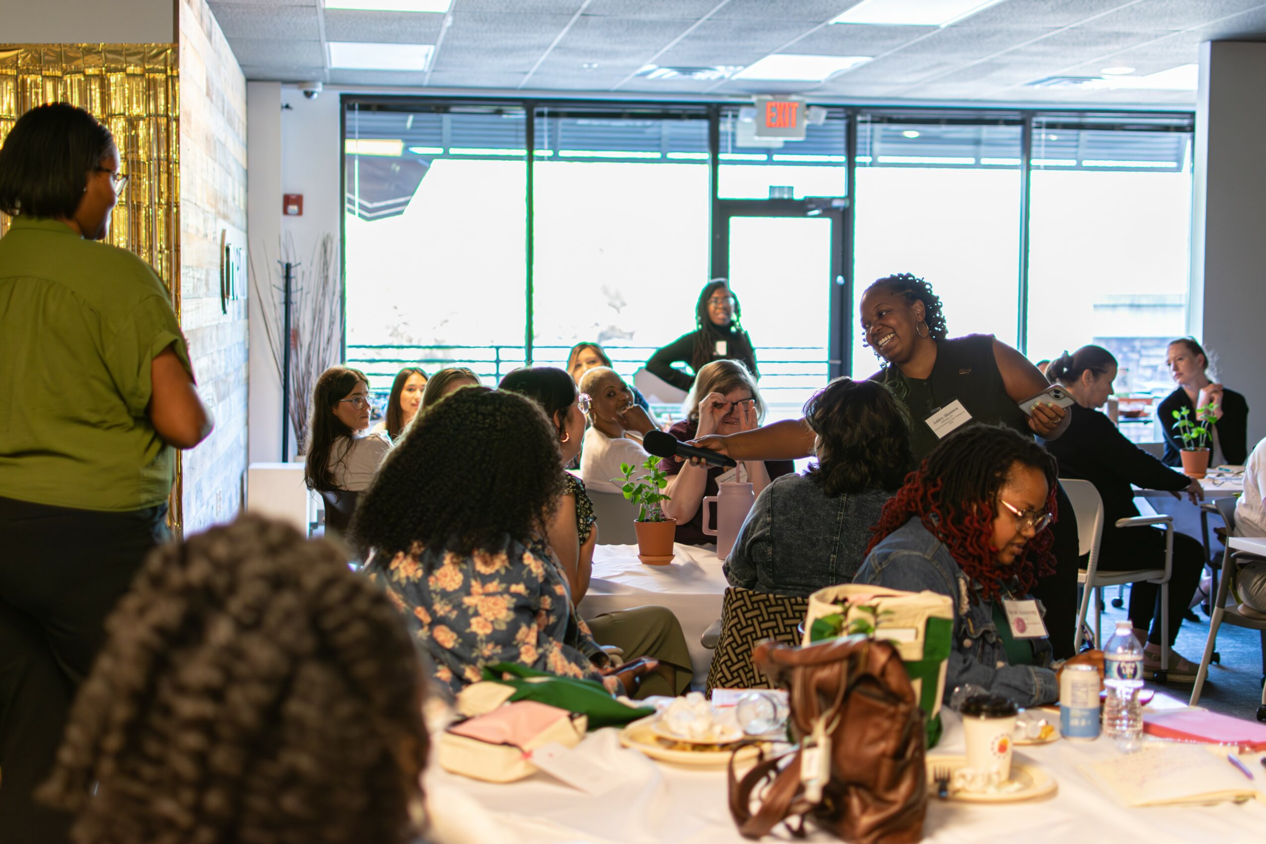 People sitting at tables in a bright indoor space with large windows, engaging in conversation and activities.