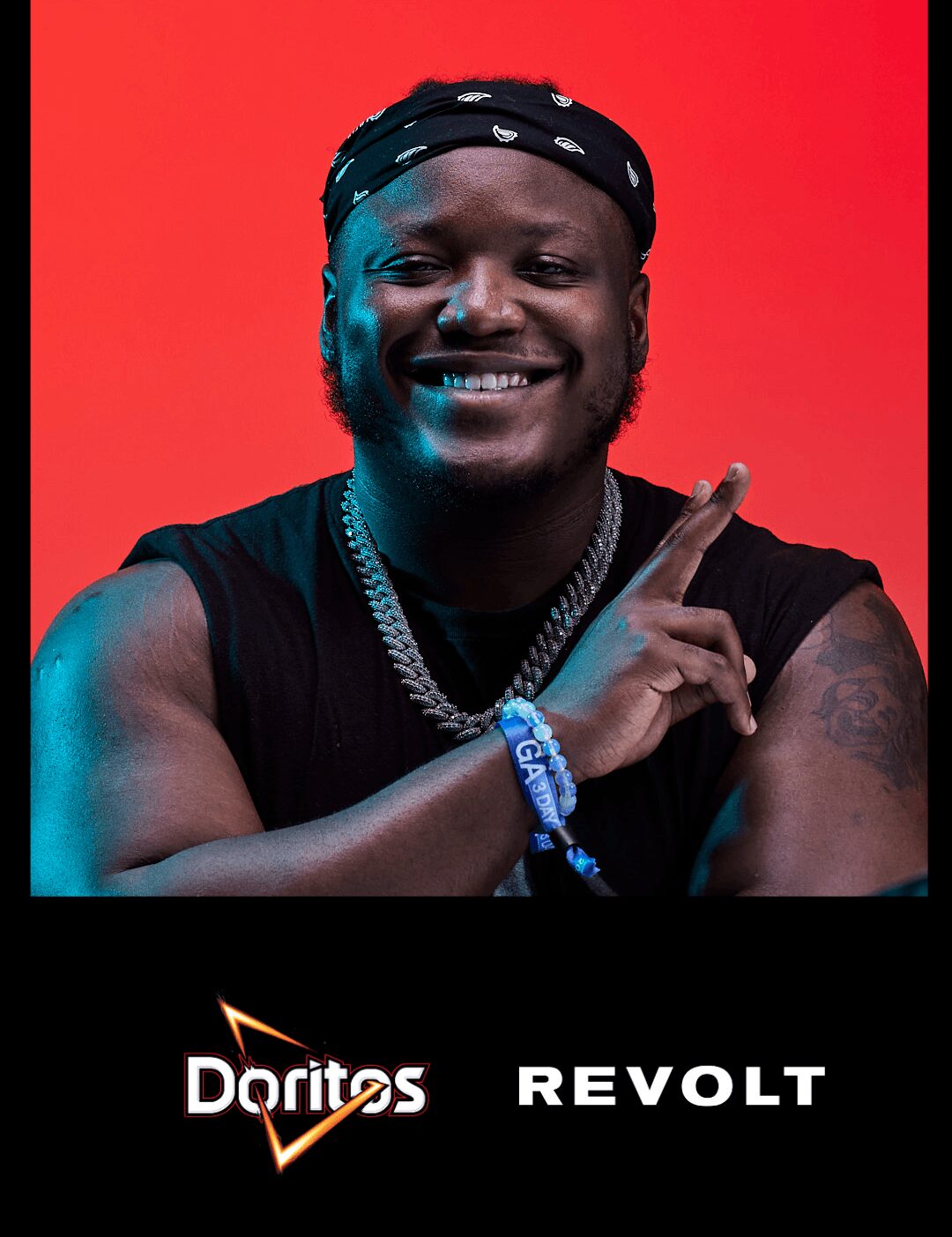 Person smiling, wearing a bandana and jewelry, pointing upward, against a red background.