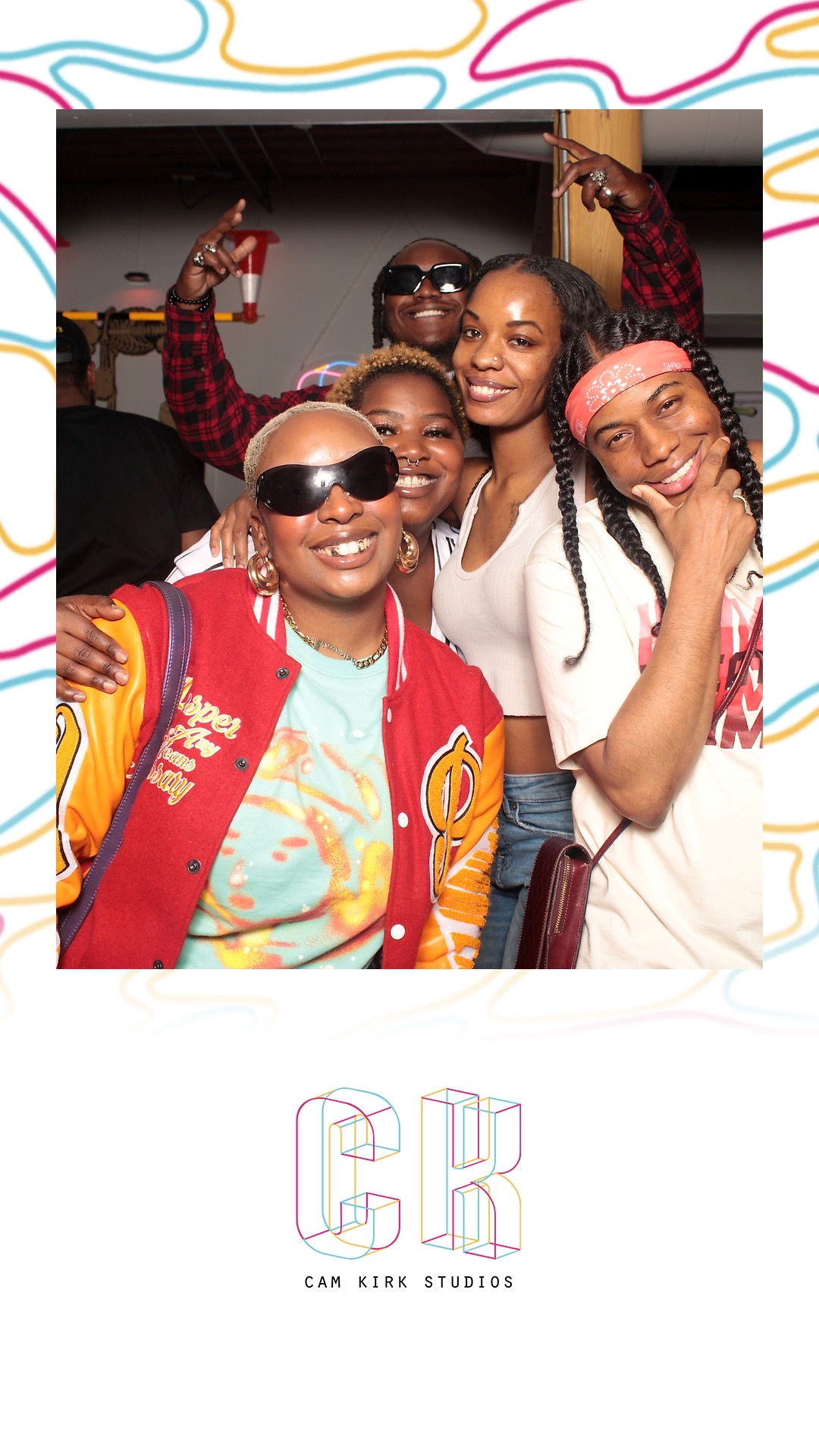 Group of five smiling people taking a selfie, wearing casual clothes and sunglasses, in a lively setting.