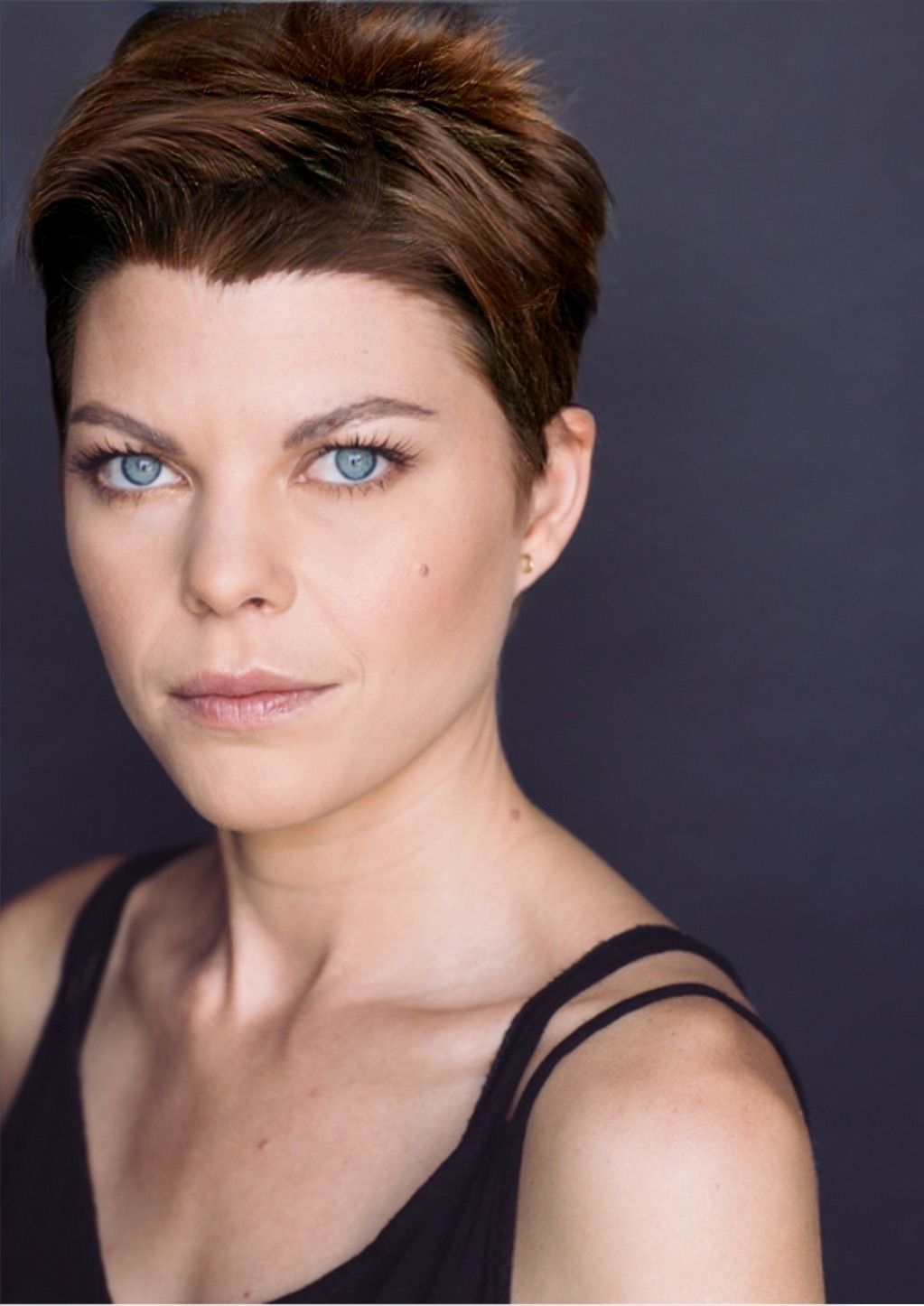 Woman with short brown hair and blue eyes looking at camera against dark background.