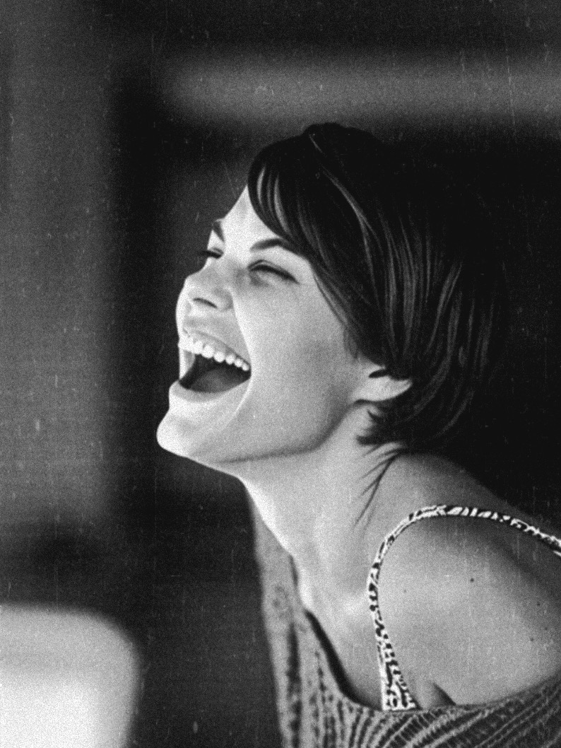 Woman with short hair laughing, head tilted back, in black and white.