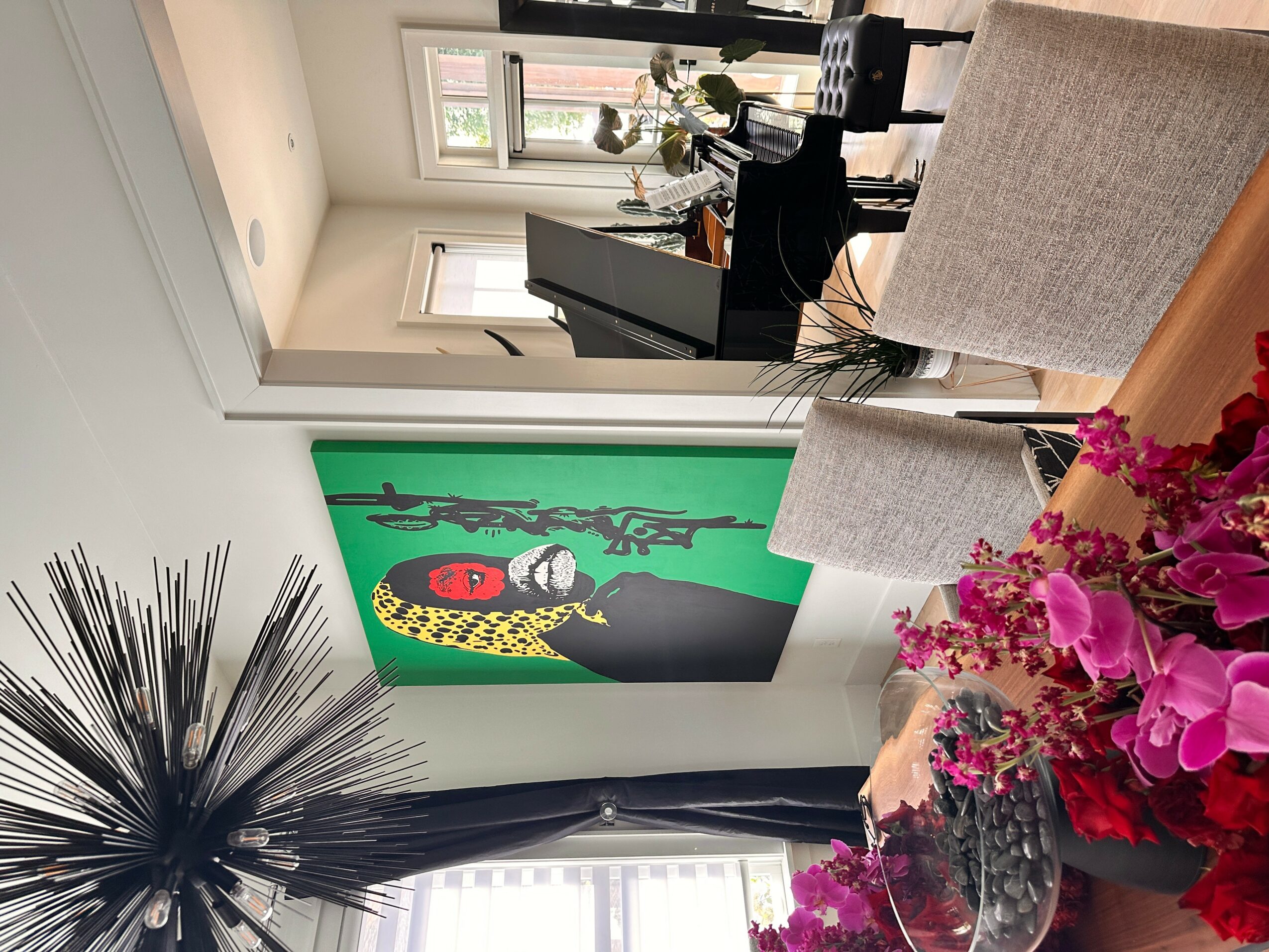 Living room with a colorful painting on the wall, a window with curtains, and a table with pink flowers.