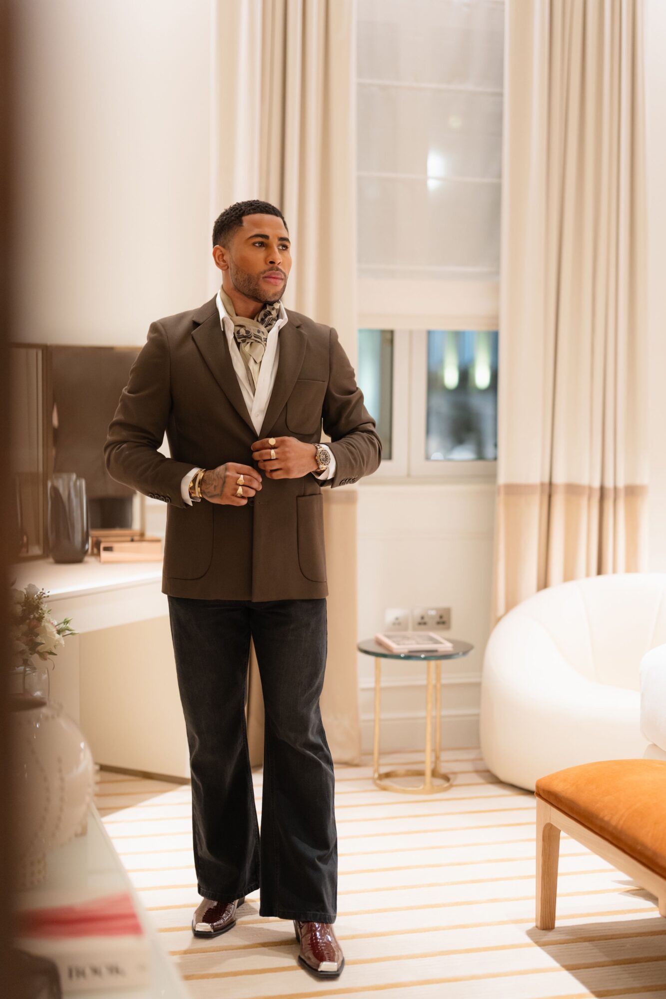 Man in suit standing in a well-lit room with large windows and modern furniture.