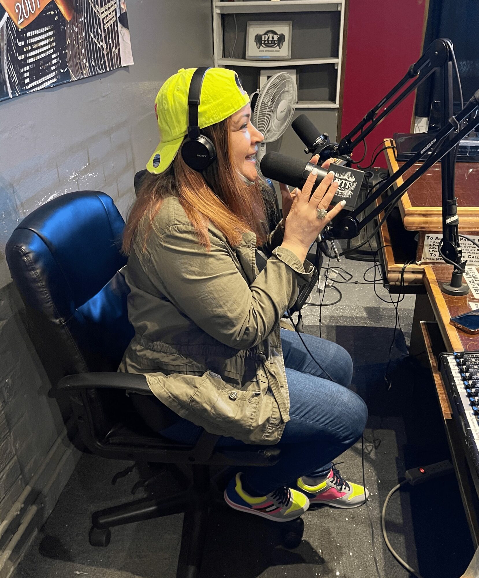 Woman wearing a yellow cap and headphones speaking into a microphone in a radio studio.