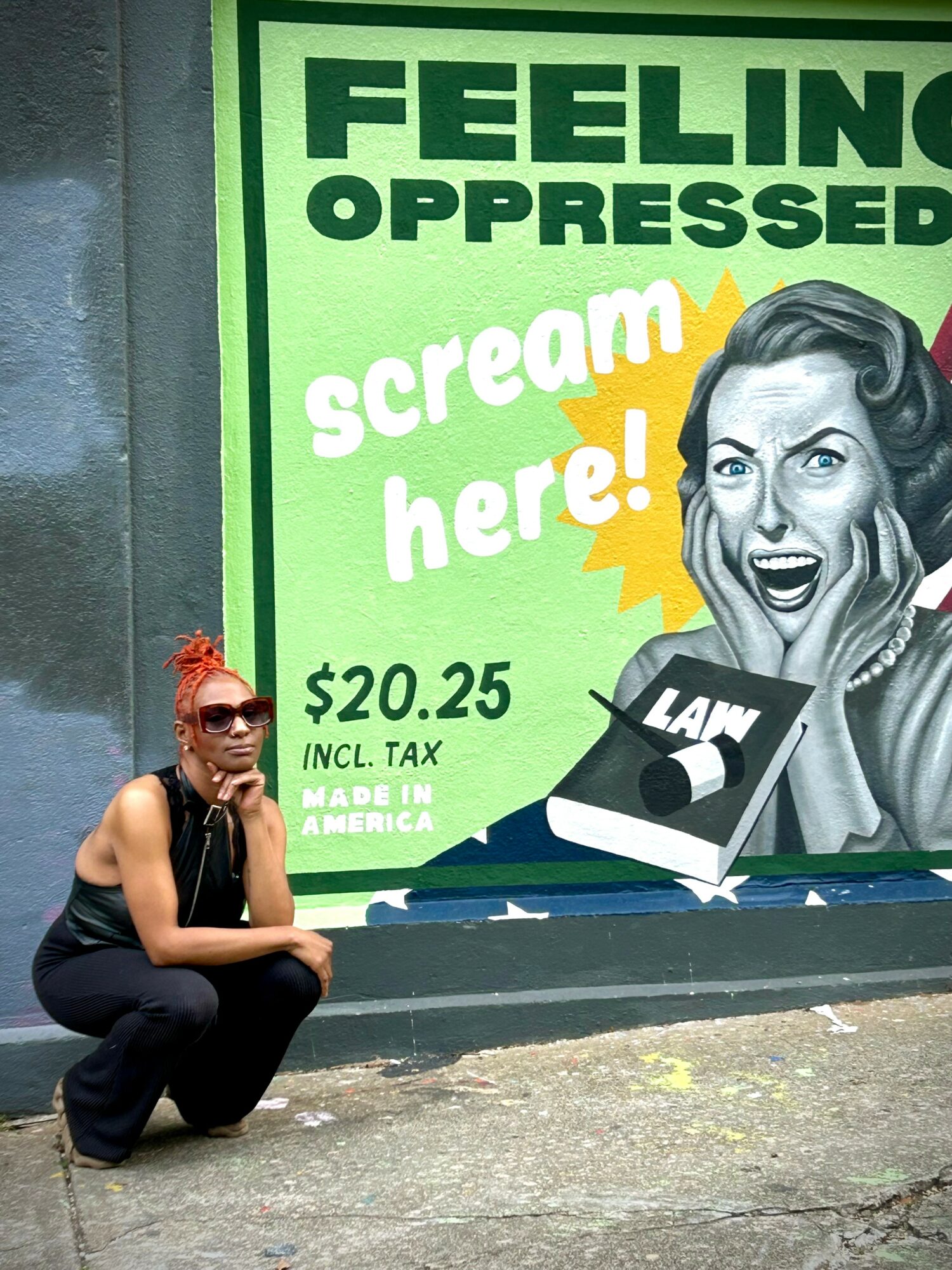 Person crouching in front of a colorful protest sign with a woman screaming and a book illustration.