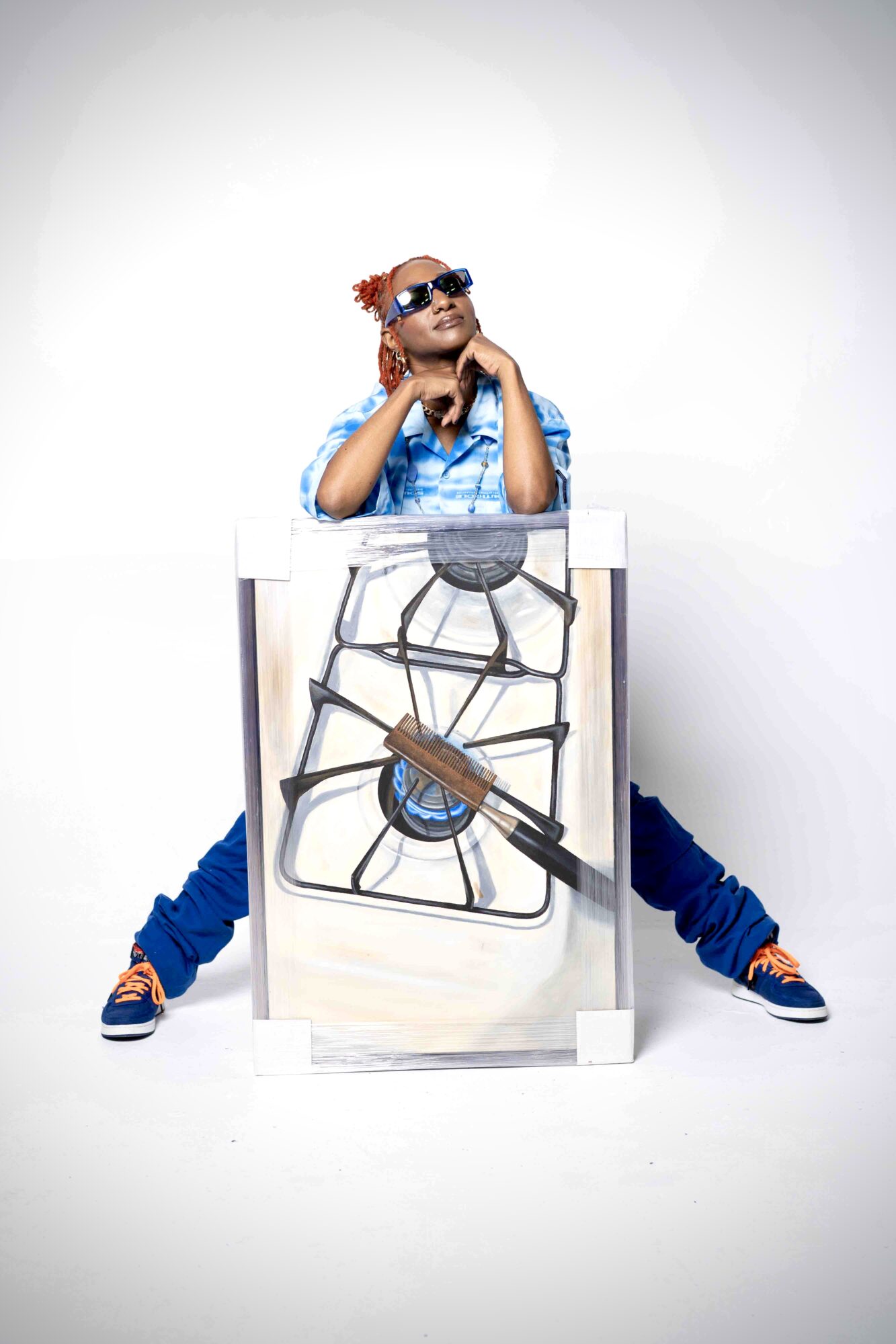 Child with sunglasses and colorful clothing sits behind a large stove illustration, with legs spread apart and hands on chin.