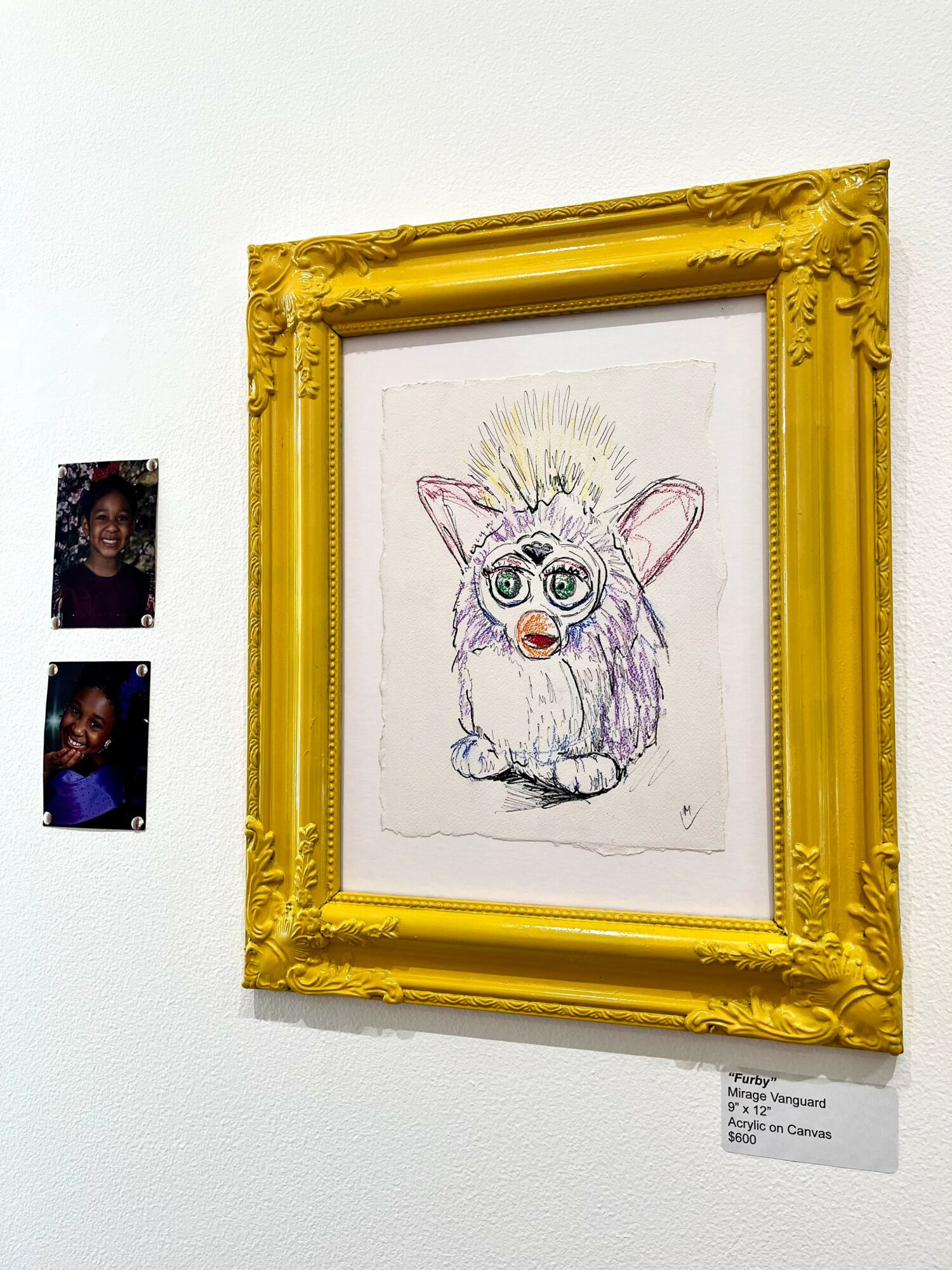 Colorful drawing of a fluffy creature with large eyes, framed in an ornate yellow frame, hanging on a white wall.