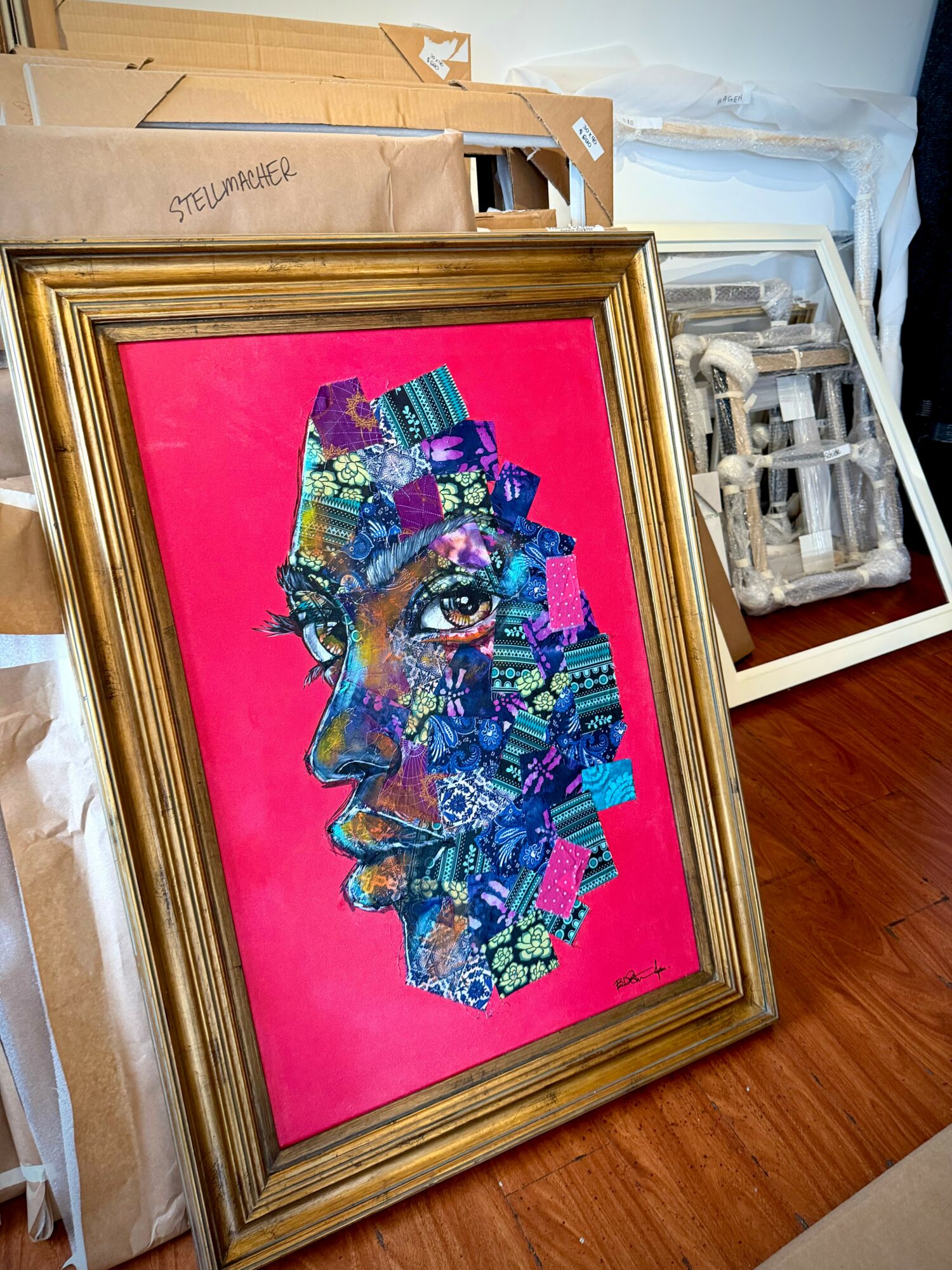 Framed colorful abstract portrait of a person's face with pink background, leaning against a wall.