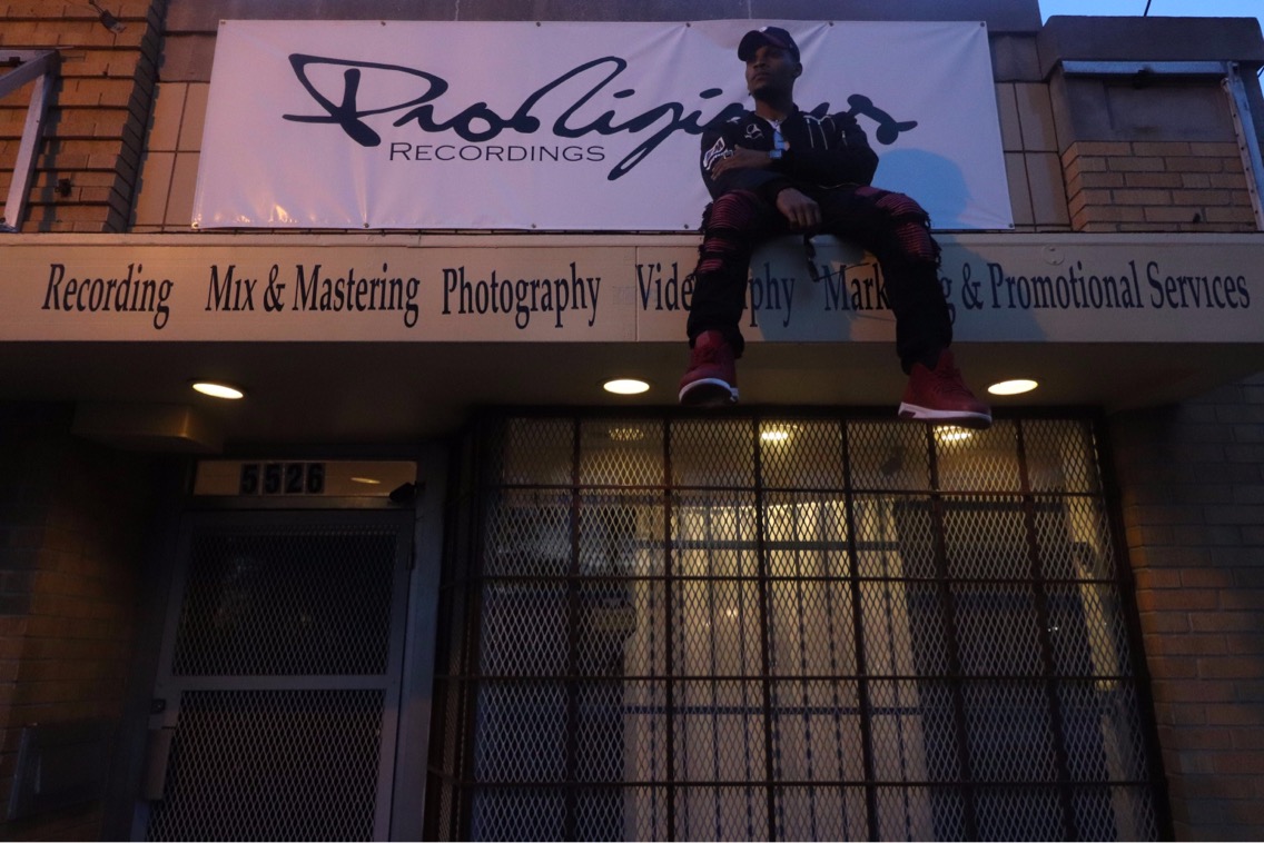 Person sitting on a ledge above a storefront with a sign for recording and production services.